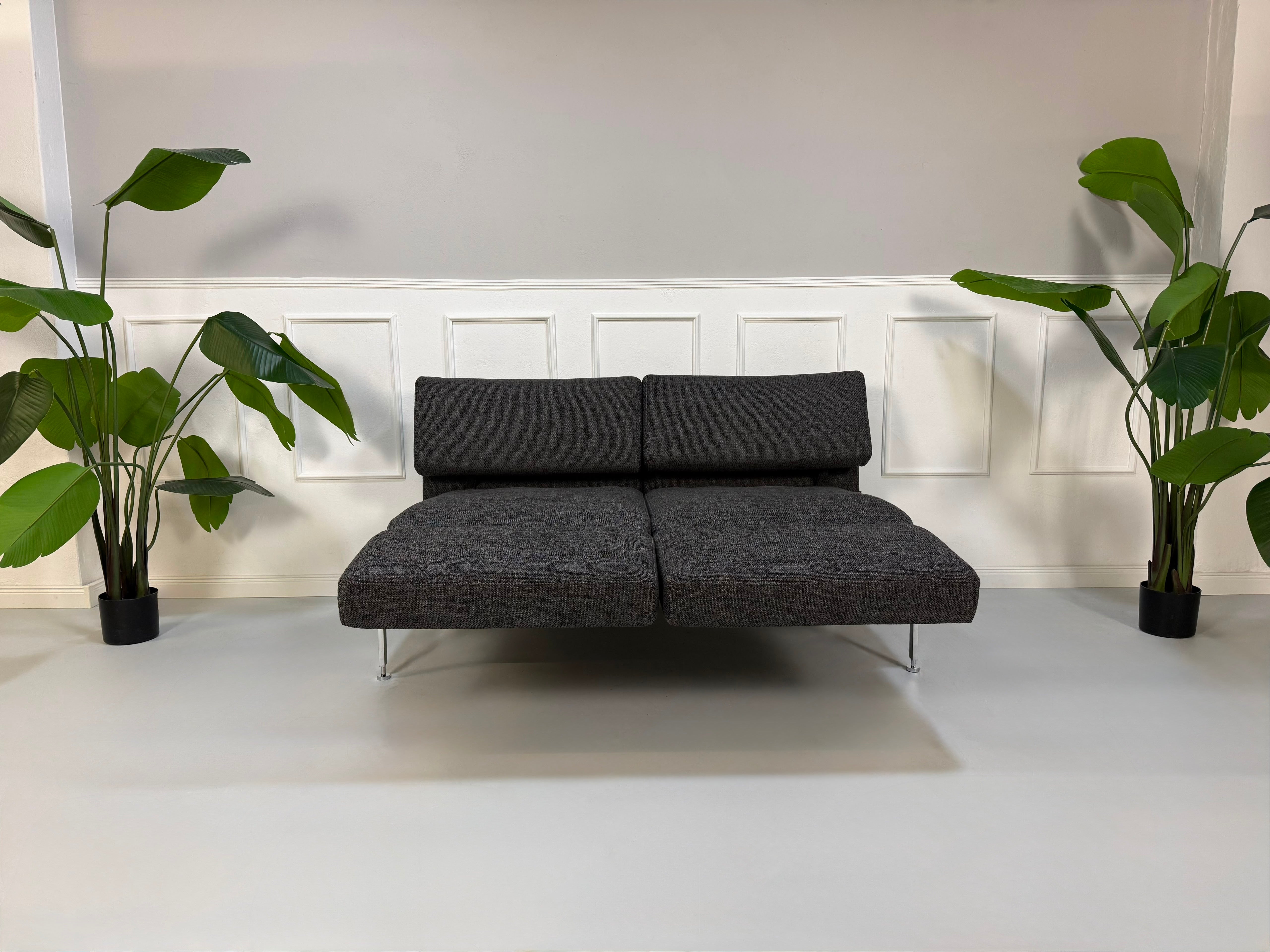 Gebrauchtes graues Brühl Roro Soft Designer Stoff Sofa vor einer Wand, stilvoll und modern eingerichtet.