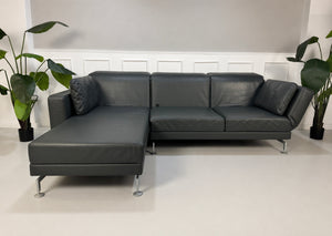 Gebrauchtes Grau Grün Brühl Moule Designer Leder Sofa vor einer Wand, stilvoll und modern eingerichtet.