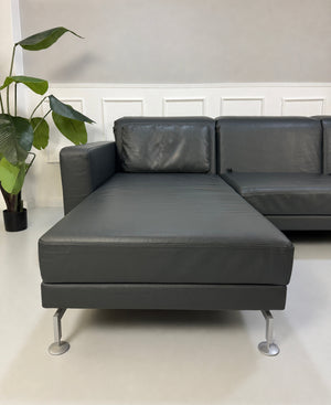 Gebrauchtes Grau Grün Brühl Moule Designer Leder Sofa vor einer Wand, stilvoll und modern eingerichtet.