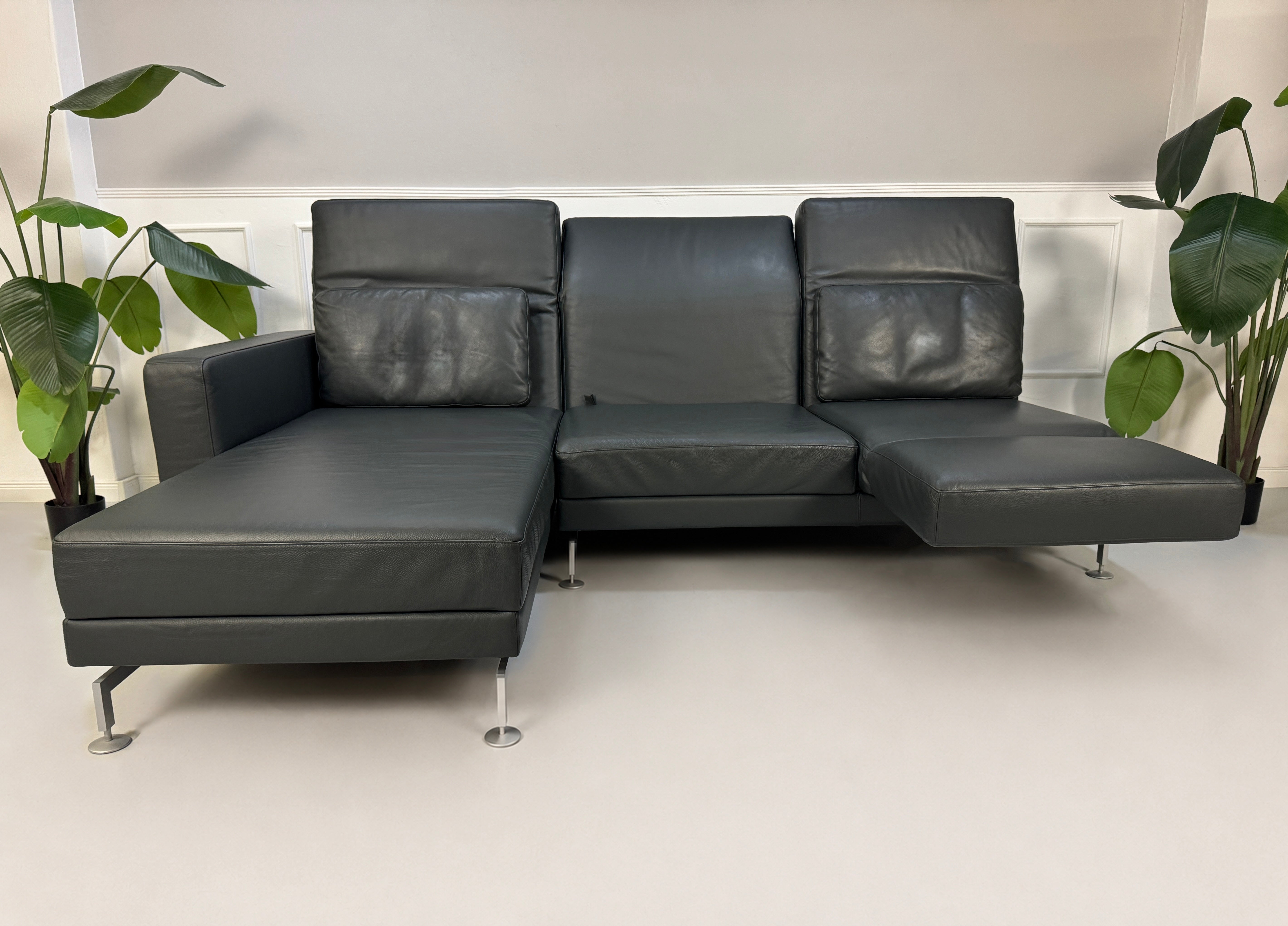 Gebrauchtes Grau Grün Brühl Moule Designer Leder Sofa vor einer Wand, stilvoll und modern eingerichtet.