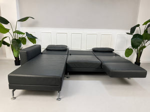 Gebrauchtes Grau Grün Brühl Moule Designer Leder Sofa vor einer Wand, stilvoll und modern eingerichtet.
