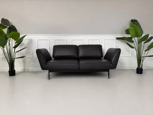 Gebrauchtes Schwarz Braun Rolf Benz Mera Designer Leder Sofa vor einer Wand, stilvoll und modern eingerichtet.