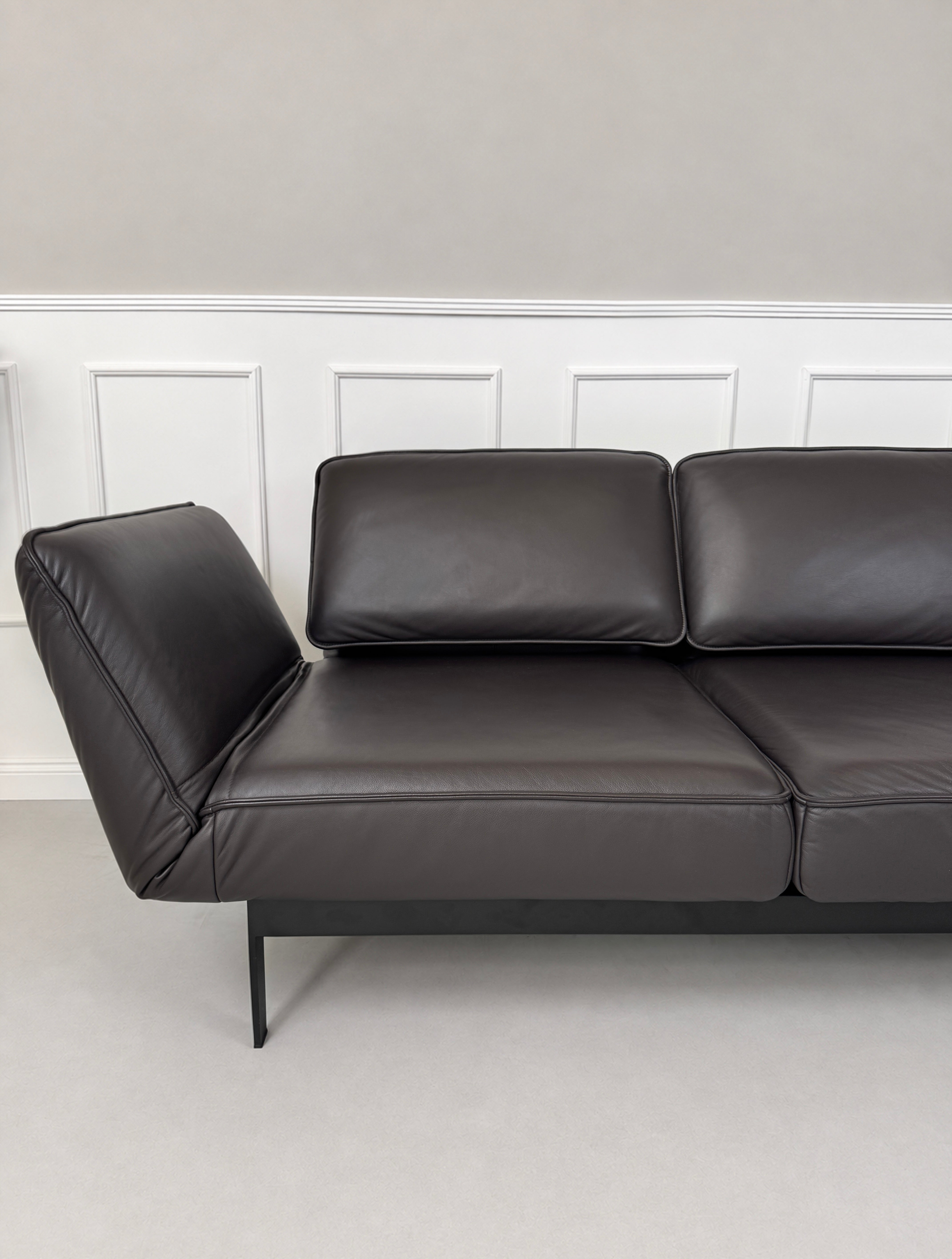 Gebrauchtes schwarz-braunes Rolf Benz Mera Designer Leder Sofa vor einer Wand, stilvoll und modern eingerichtet.
