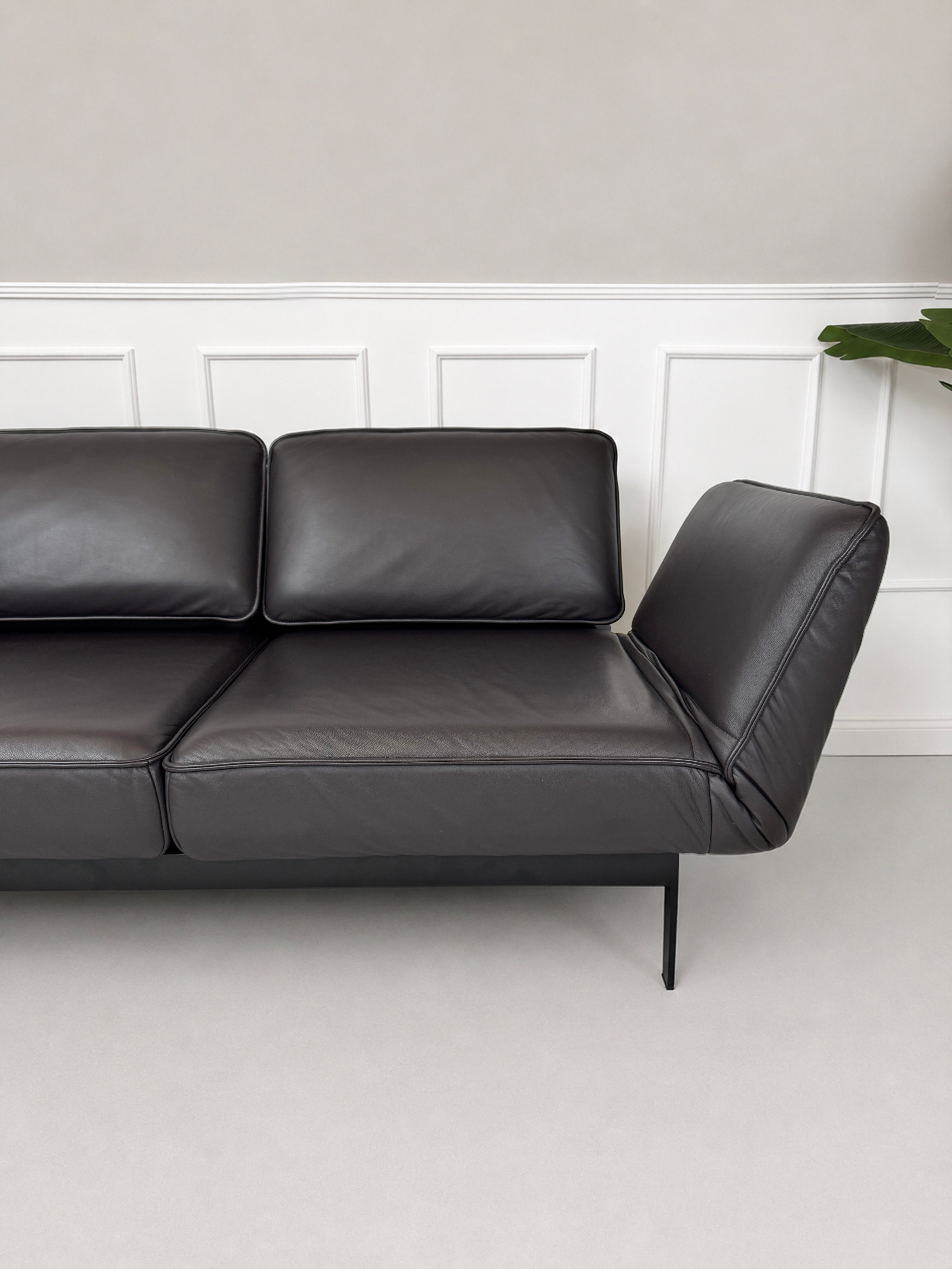 Gebrauchtes schwarz-braunes Rolf Benz Mera Designer Leder Sofa vor einer Wand, stilvoll und modern eingerichtet.