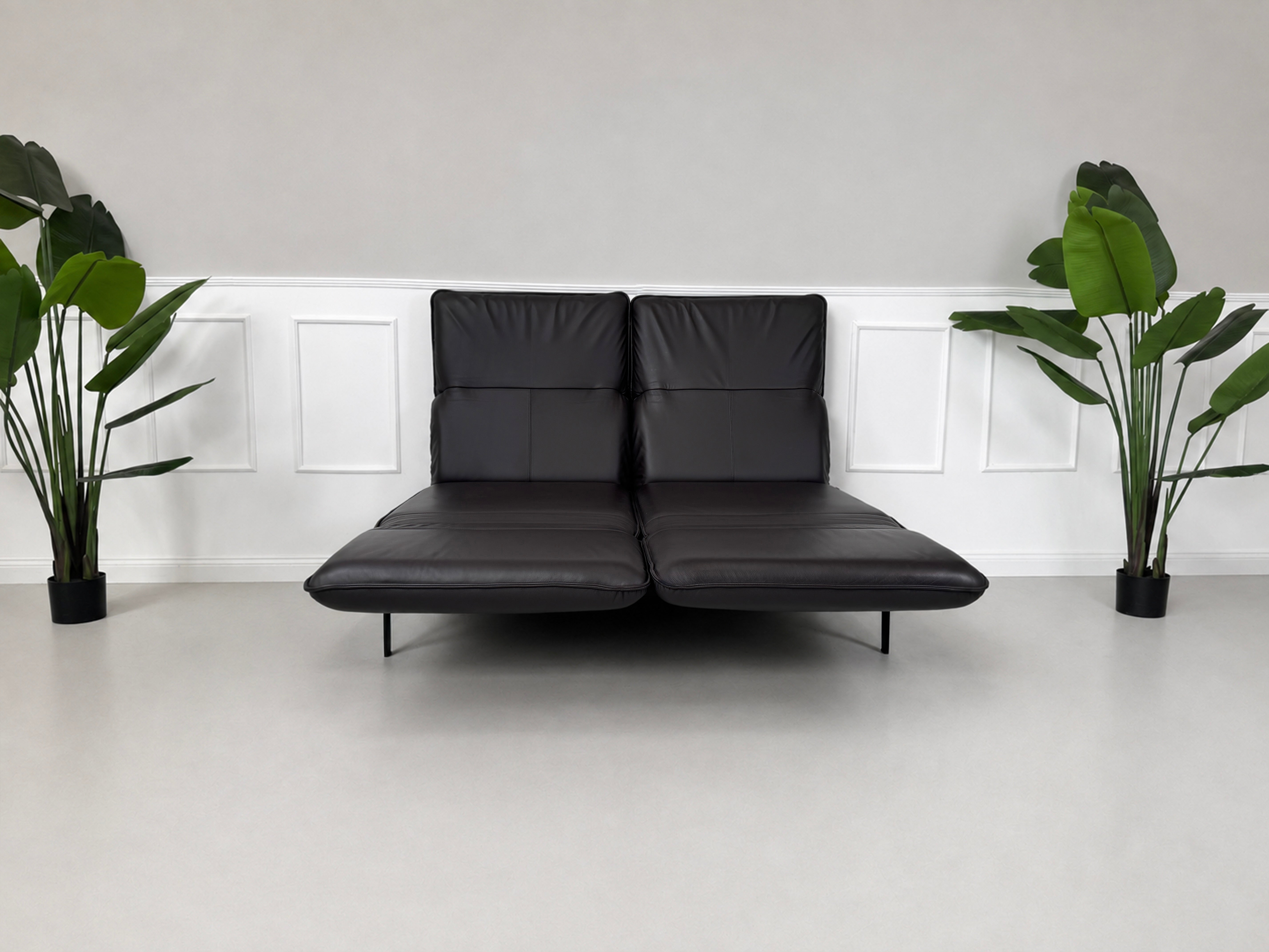 Gebrauchtes schwarz-braunes Rolf Benz Mera Designer Leder Sofa vor einer Wand, stilvoll und modern eingerichtet.