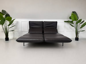 Gebrauchtes schwarz-braunes Rolf Benz Mera Designer Leder Sofa vor einer Wand, stilvoll und modern eingerichtet.