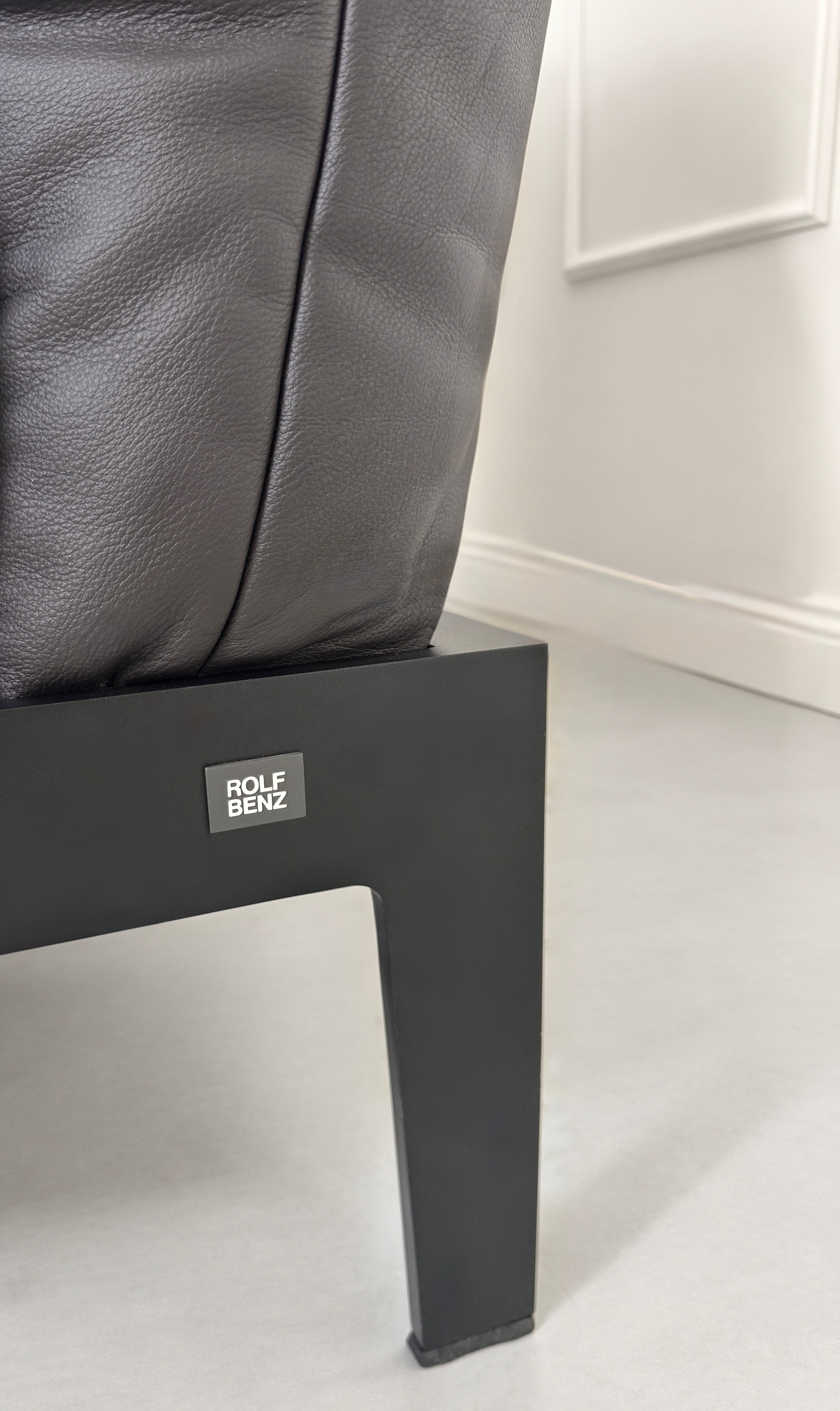 Gebrauchtes schwarz-braunes Rolf Benz Mera Designer Leder Sofa vor einer Wand, stilvoll und modern eingerichtet.