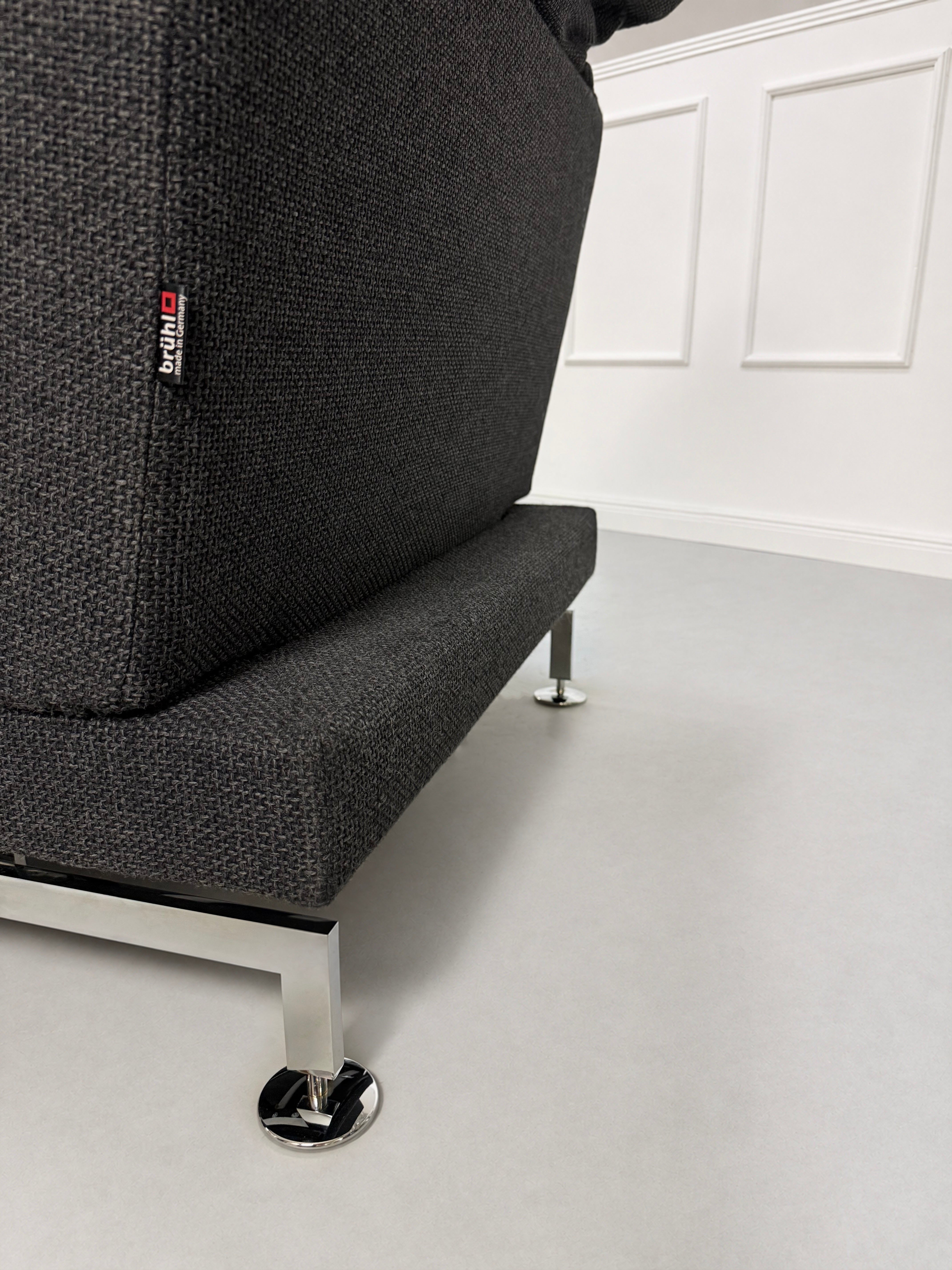 Gebrauchtes graues Brühl Moule Designer Stoff Sofa vor einer Wand, stilvoll und modern eingerichtet.