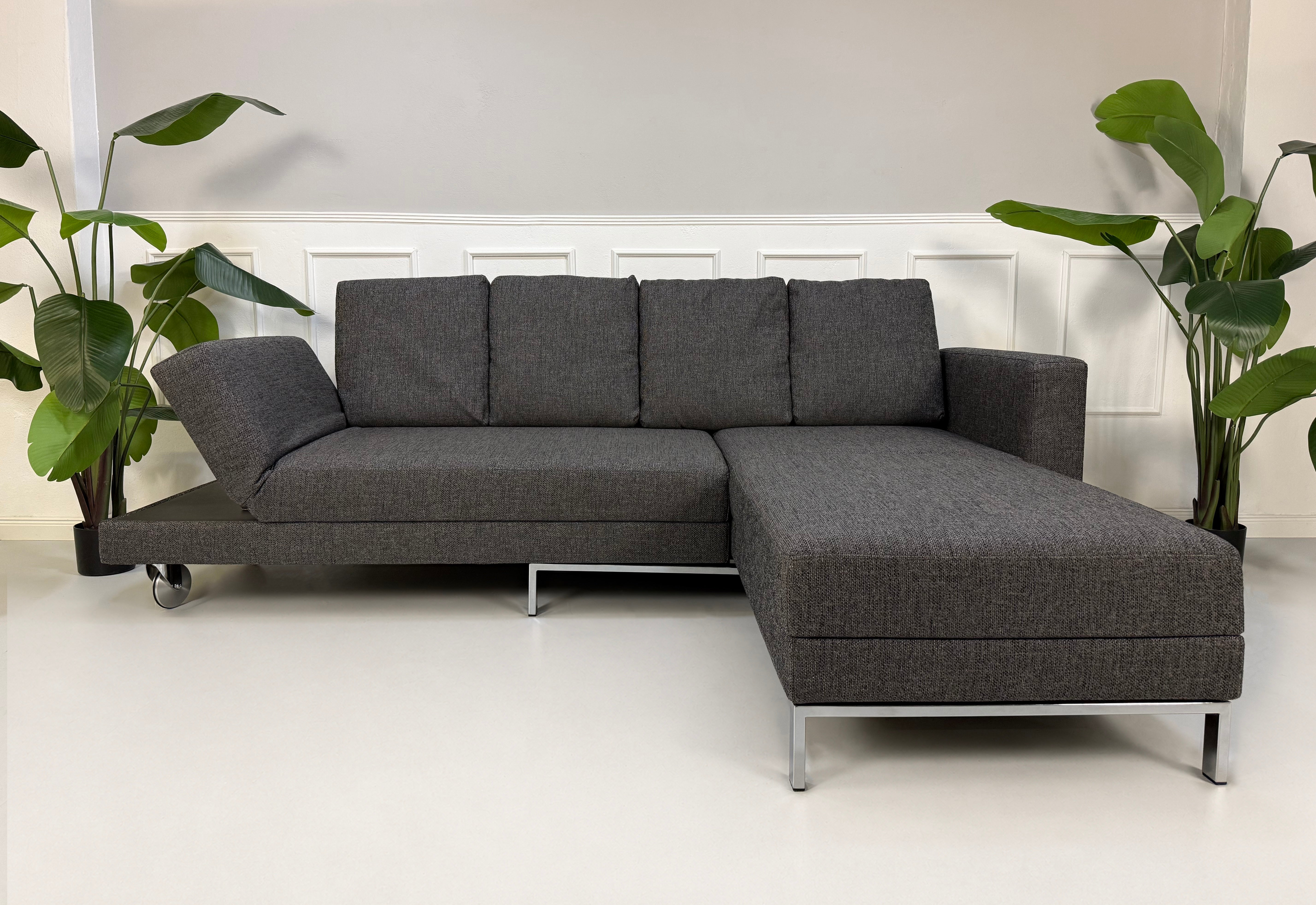 Gebrauchtes graues Brühl Fourtwo Designer Stoff Sofa vor einer Wand, stilvoll und modern eingerichtet.