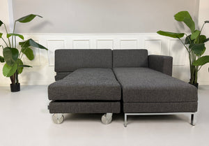 Gebrauchtes graues Brühl Fourtwo Designer Stoff Sofa vor einer Wand, stilvoll und modern eingerichtet.