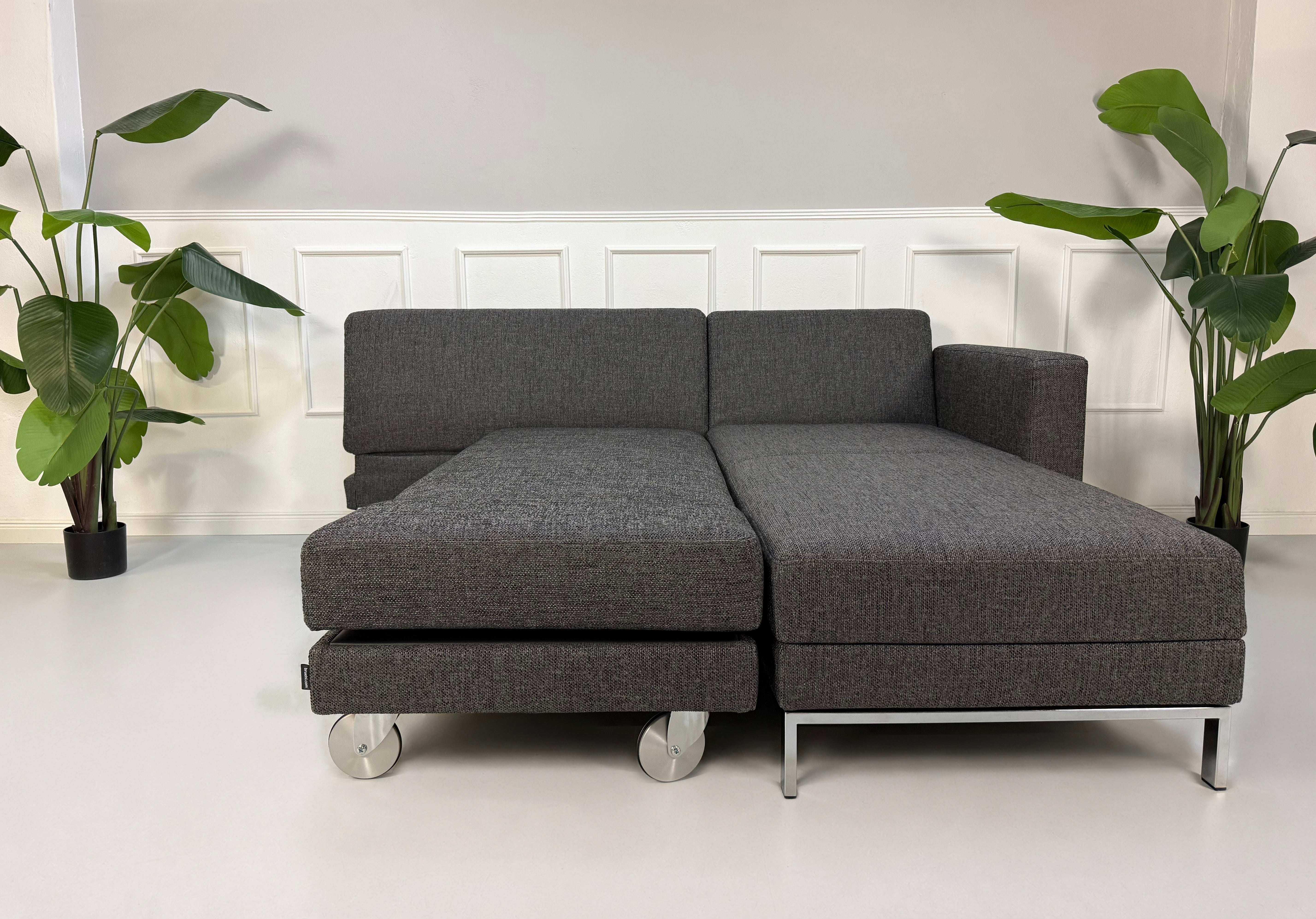 Gebrauchtes graues Brühl Fourtwo Designer Stoff Sofa vor einer Wand, stilvoll und modern eingerichtet.
