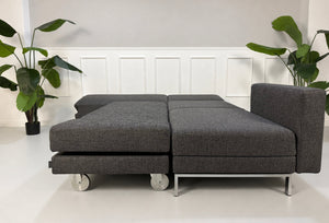 Gebrauchtes graues Brühl Fourtwo Designer Stoff Sofa vor einer Wand, stilvoll und modern eingerichtet.