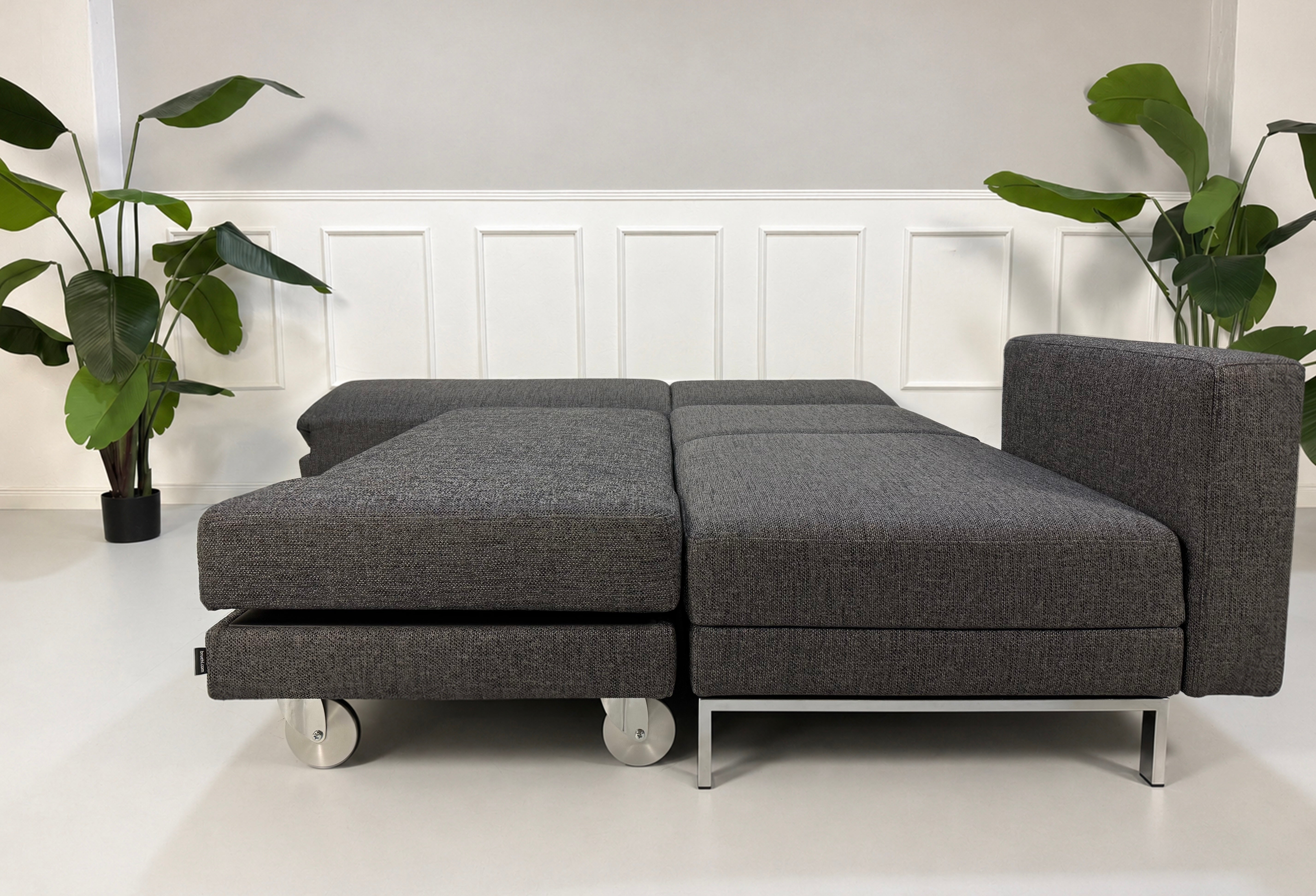 Gebrauchtes graues Brühl Fourtwo Designer Stoff Sofa vor einer Wand, stilvoll und modern eingerichtet.