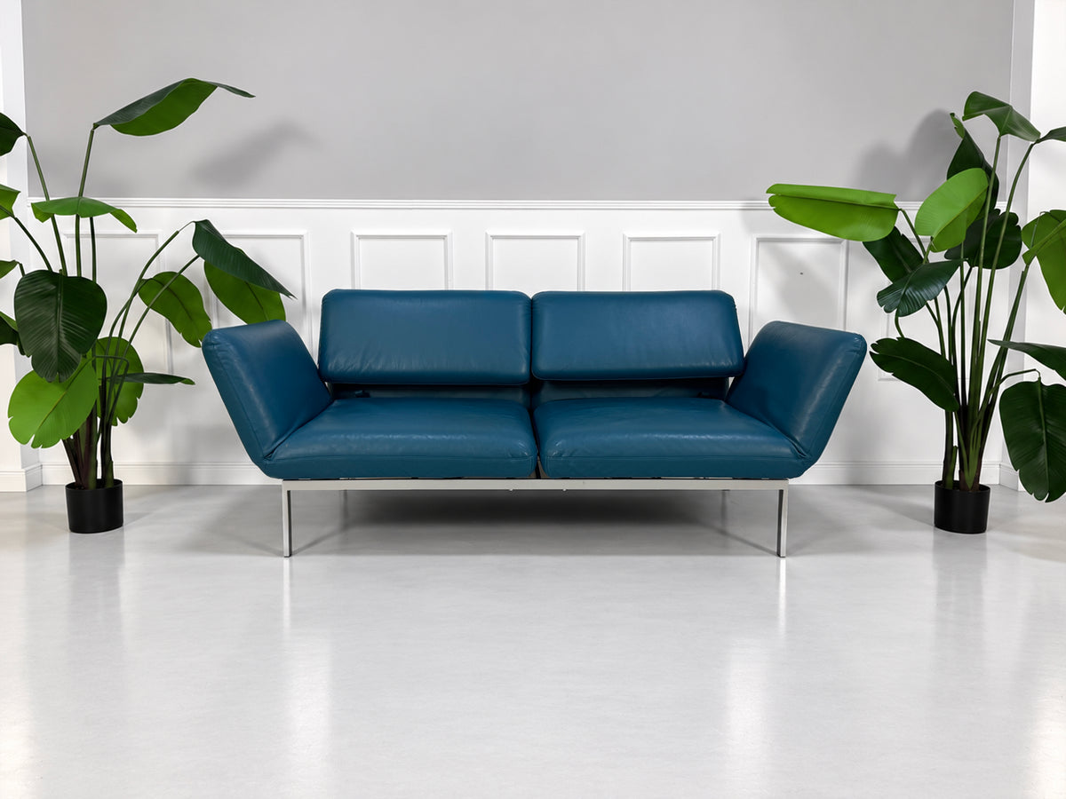 Gebrauchtes blaues Brühl Roro Medium Designer Leder Sofa vor einer Wand, stilvoll und modern eingerichtet.