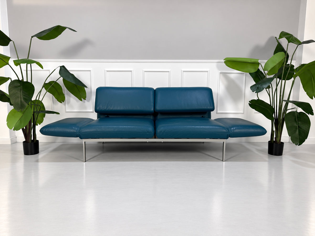 Gebrauchtes blaues Brühl Roro Medium Designer Leder Sofa vor einer Wand, stilvoll und modern eingerichtet.