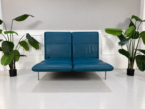 Gebrauchtes blaues Brühl Roro Medium Designer Leder Sofa vor einer Wand, stilvoll und modern eingerichtet.