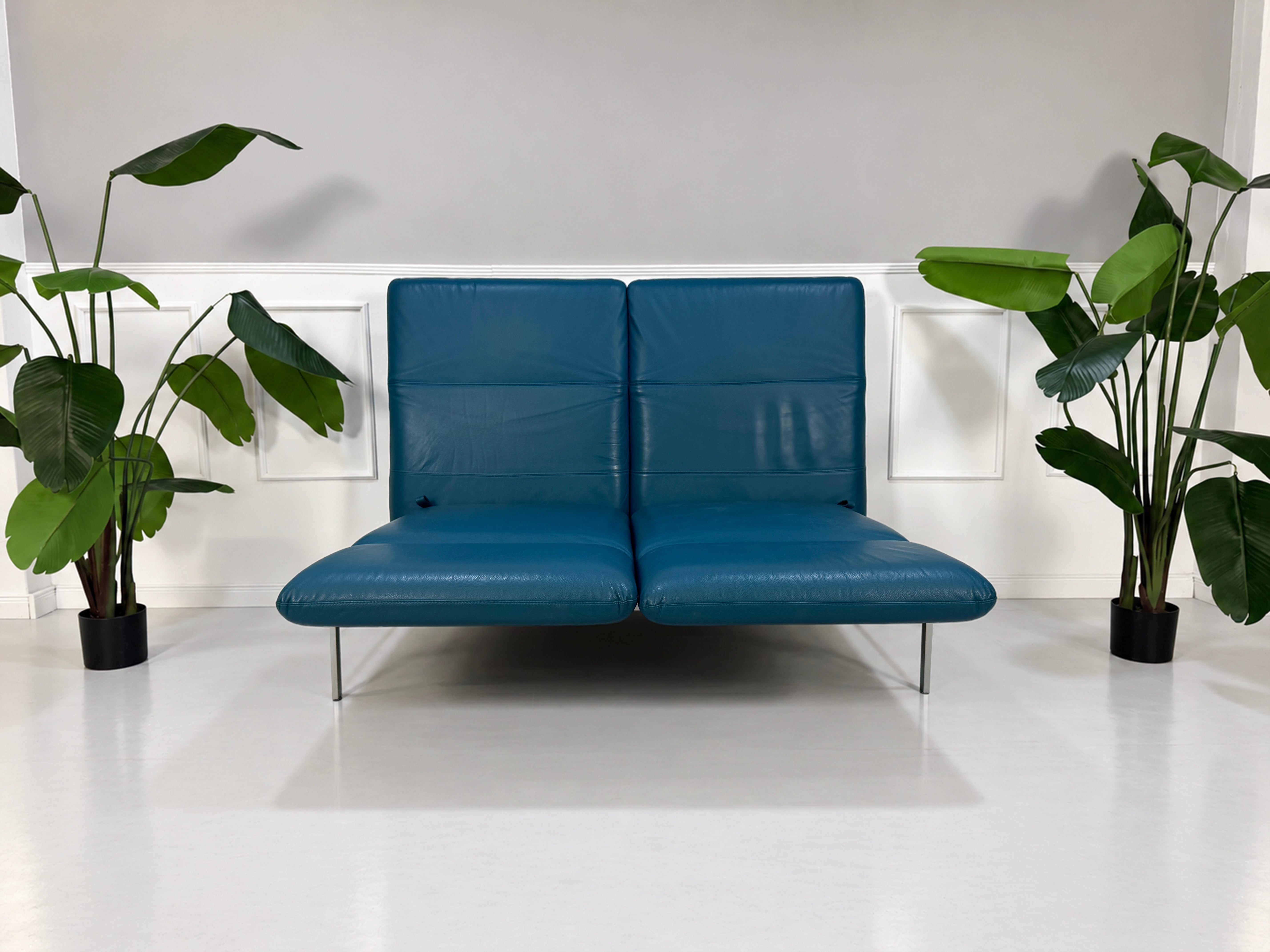 Gebrauchtes blaues Brühl Roro Medium Designer Leder Sofa vor einer Wand, stilvoll und modern eingerichtet.