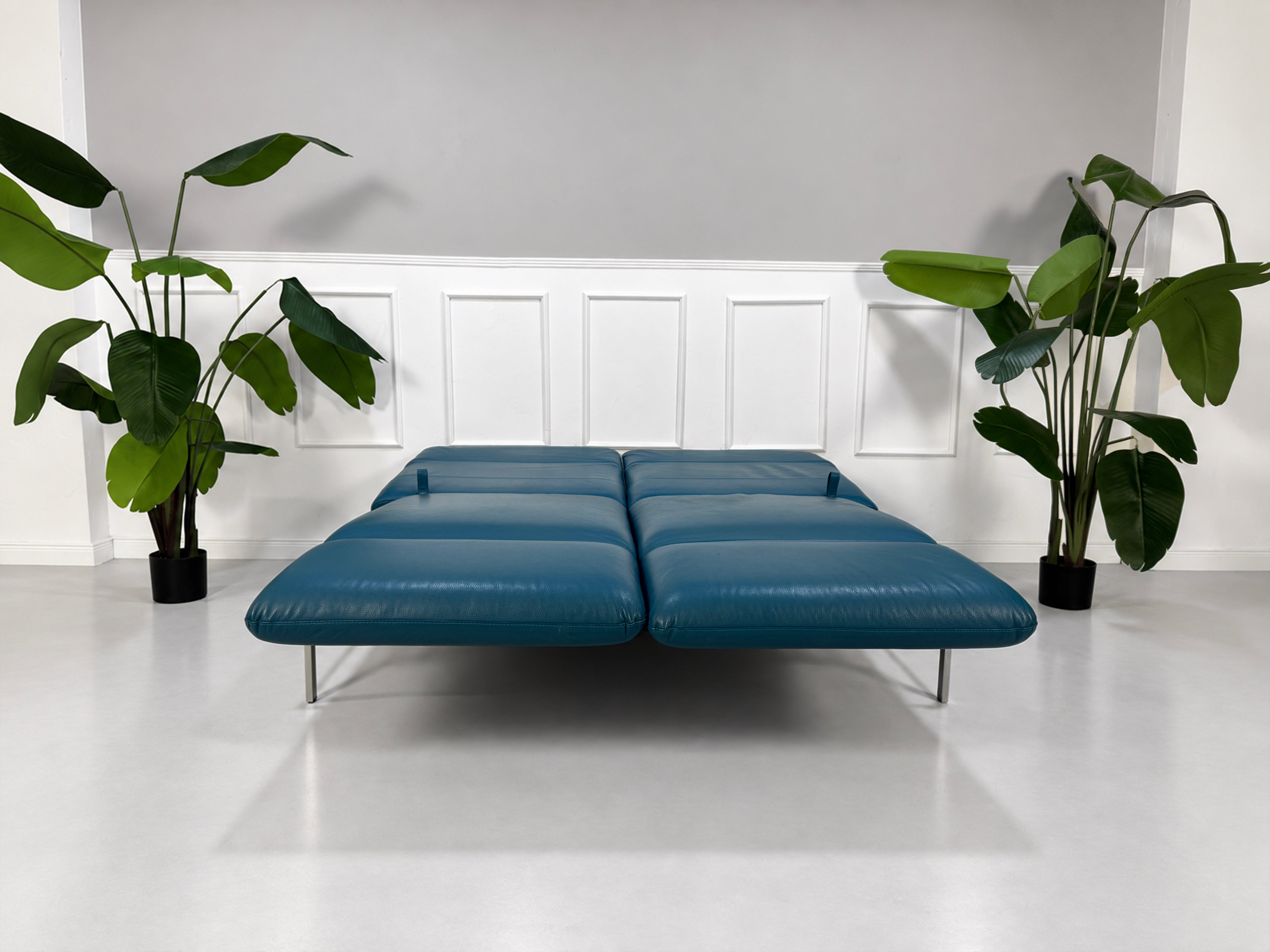 Gebrauchtes blaues Brühl Roro Medium Designer Leder Sofa vor einer Wand, stilvoll und modern eingerichtet.