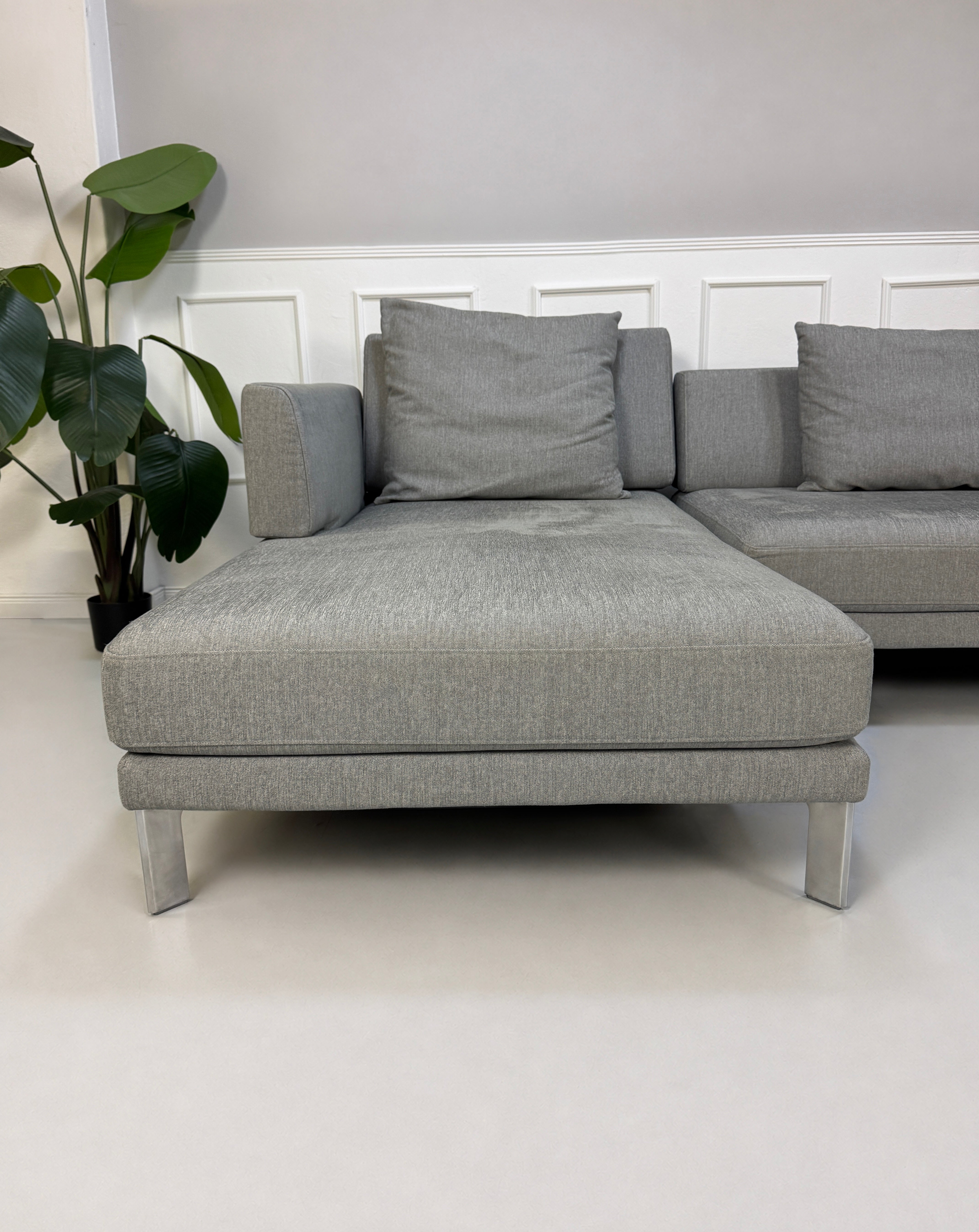 Gebrauchtes graues Rolf Benz Sento Designer Stoff Sofa vor einer Wand, stilvoll und modern eingerichtet.