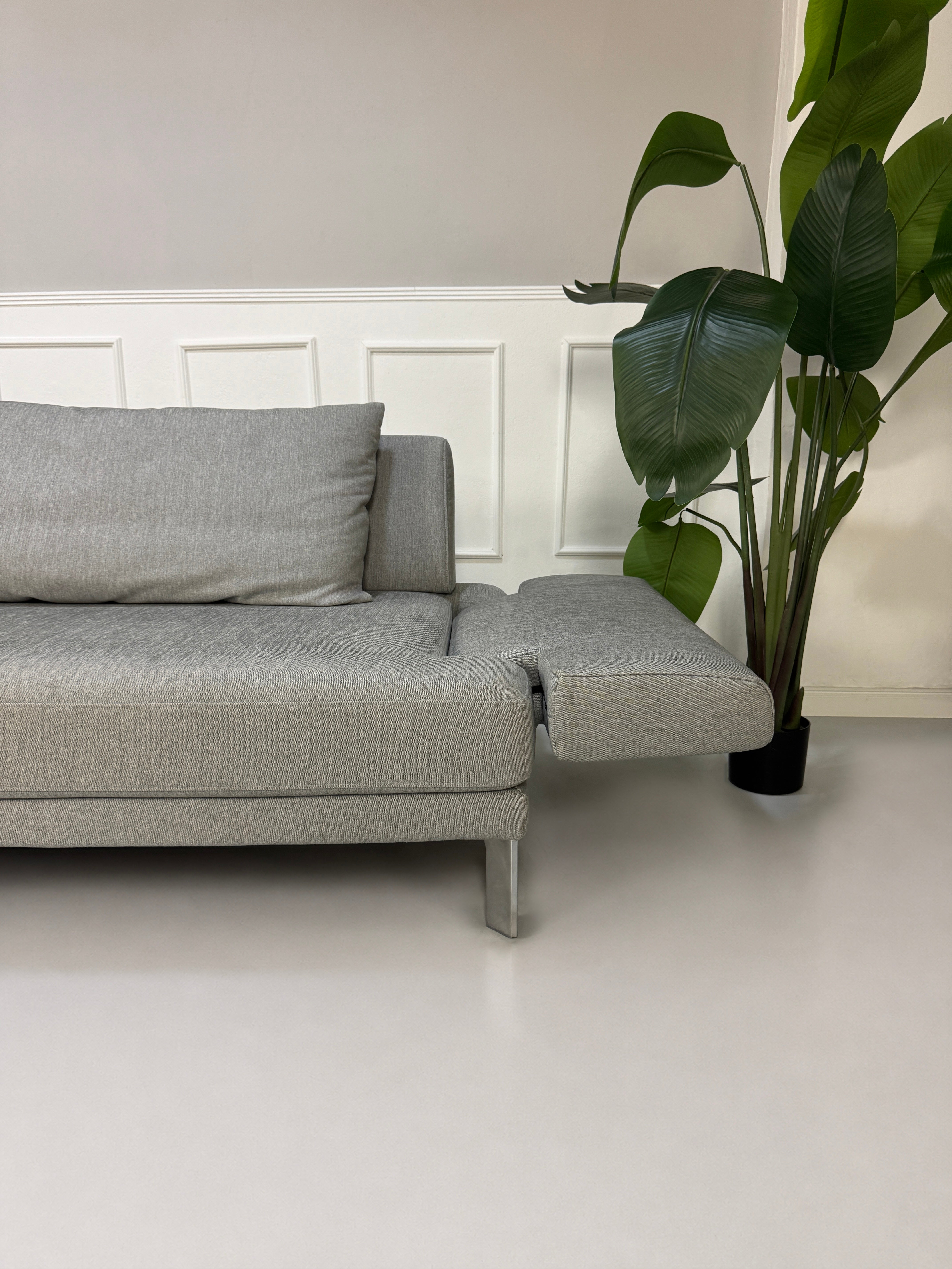 Gebrauchtes graues Rolf Benz Sento Designer Stoff Sofa vor einer Wand, stilvoll und modern eingerichtet.