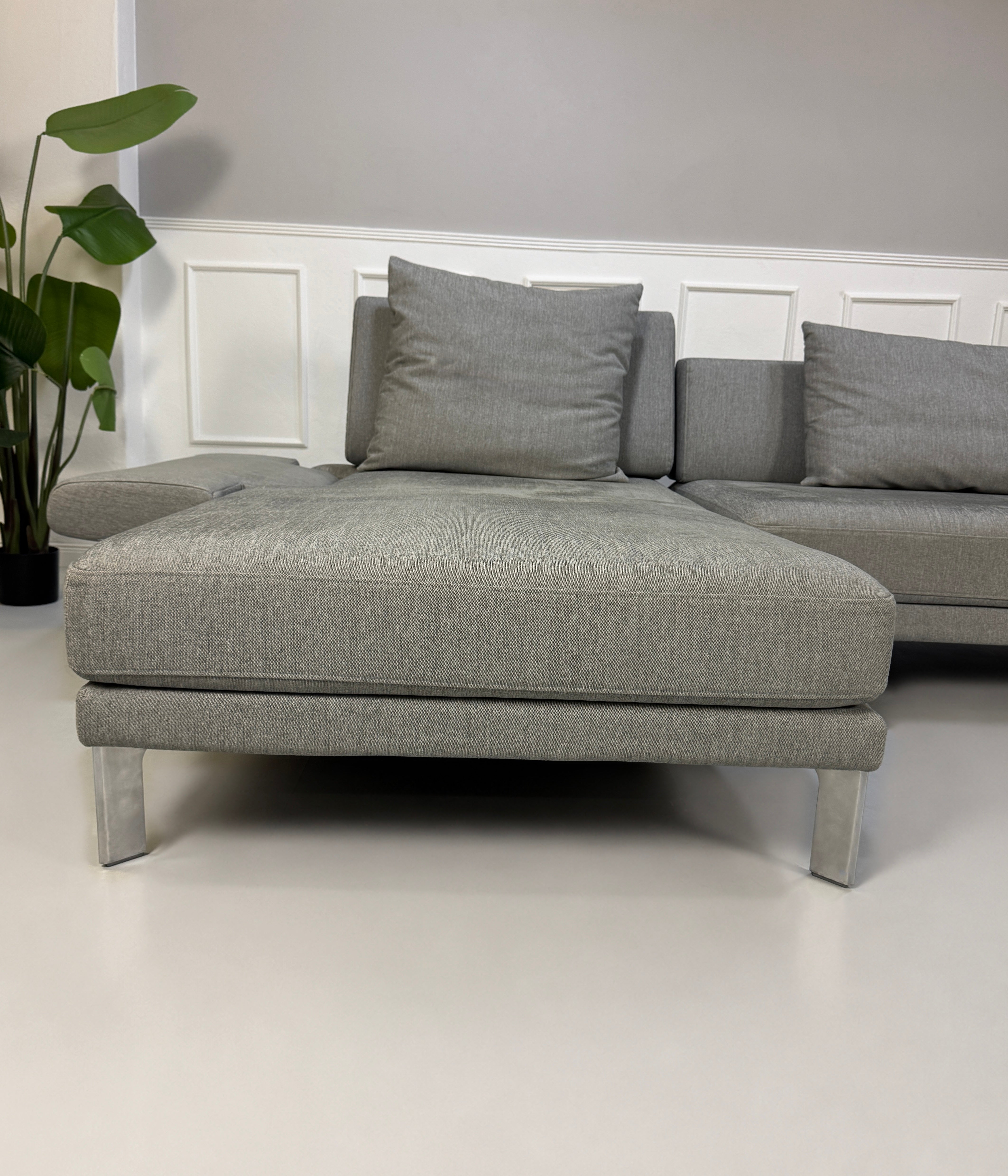 Gebrauchtes graues Rolf Benz Sento Designer Stoff Sofa vor einer Wand, stilvoll und modern eingerichtet.