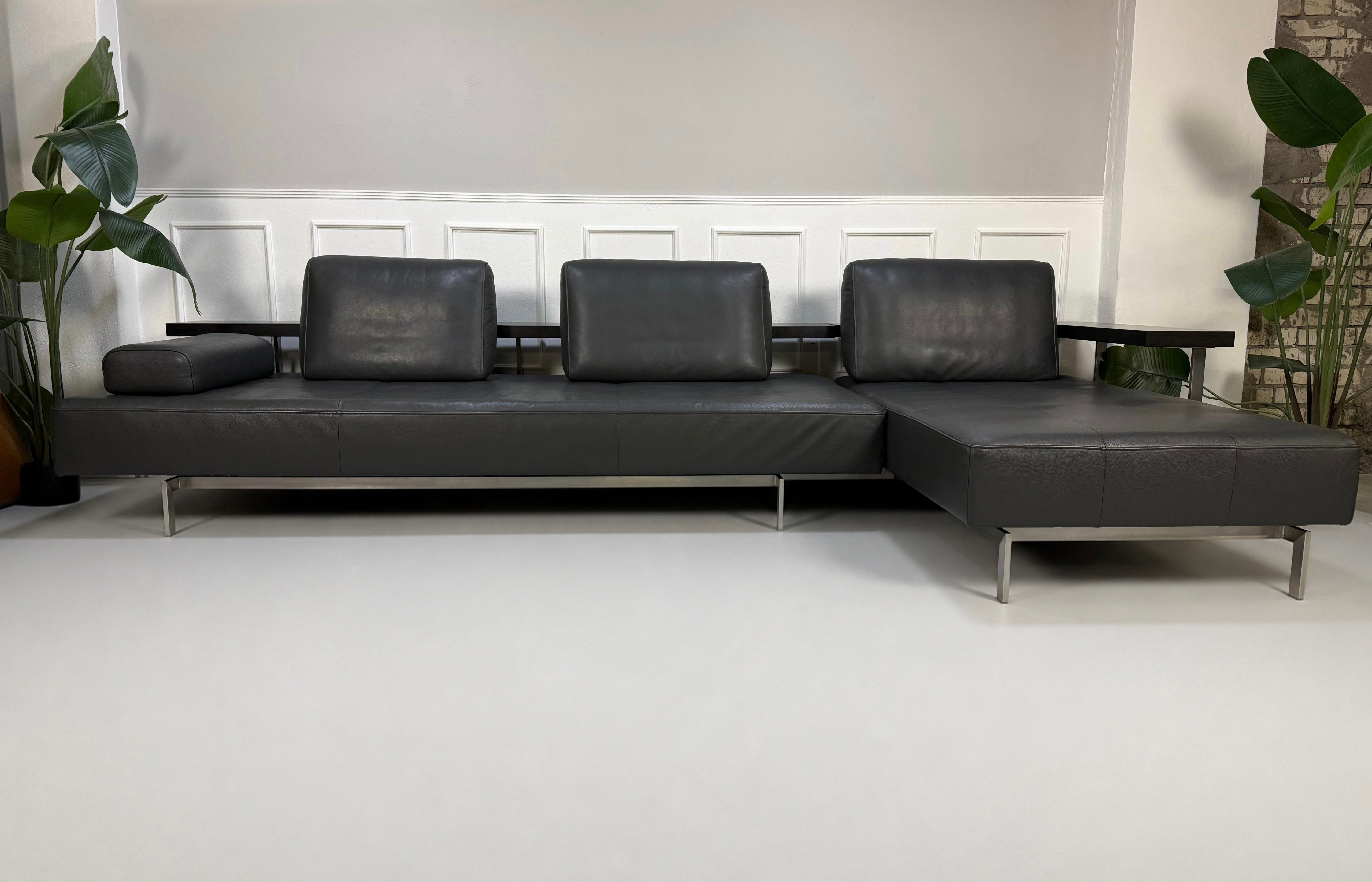 Gebrauchtes graues Rolf Benz Dono Designer Leder Sofa vor einer Wand, stilvoll und modern eingerichtet.