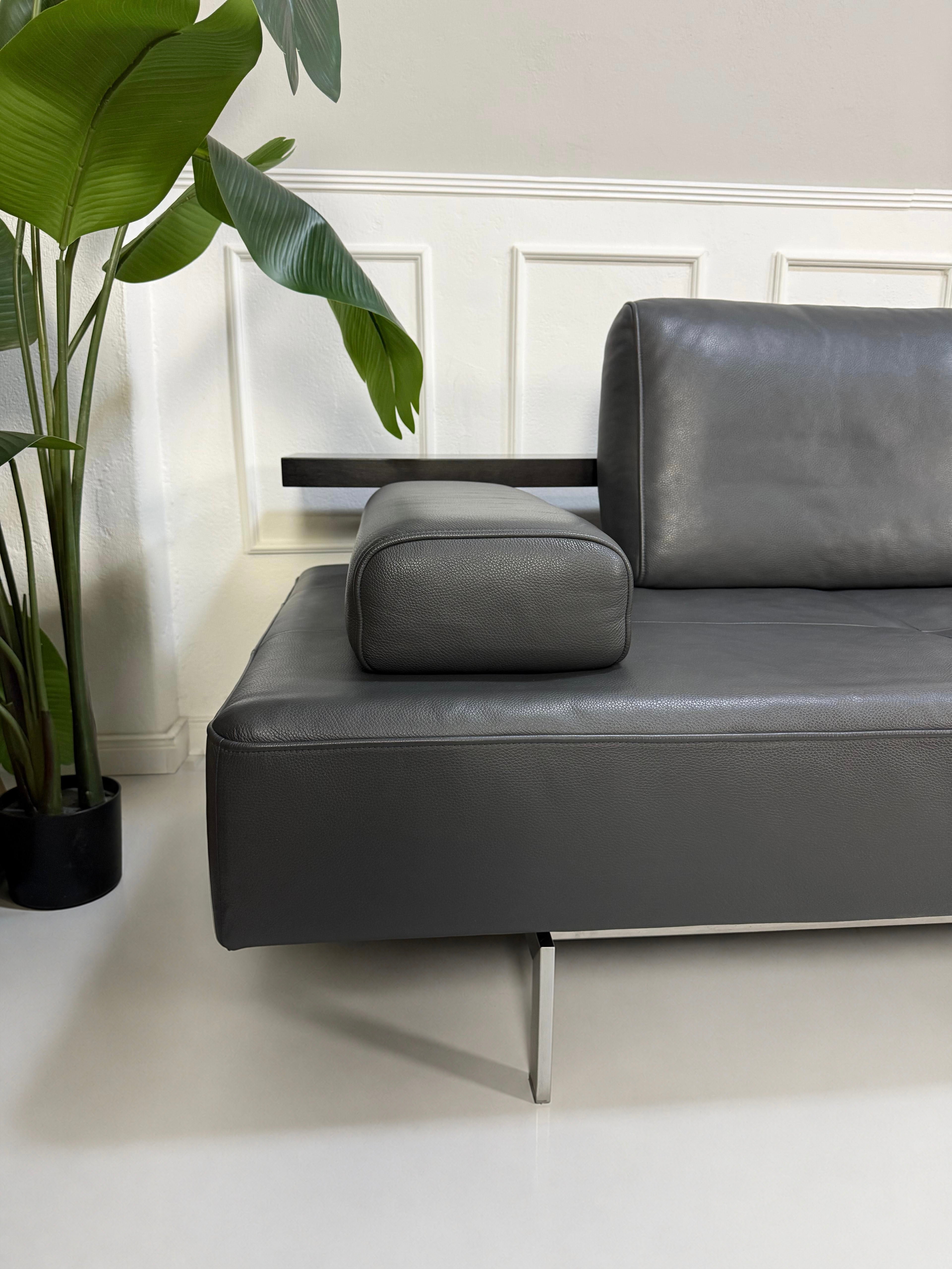 Gebrauchtes graues Rolf Benz Dono Designer Leder Sofa vor einer Wand, stilvoll und modern eingerichtet.