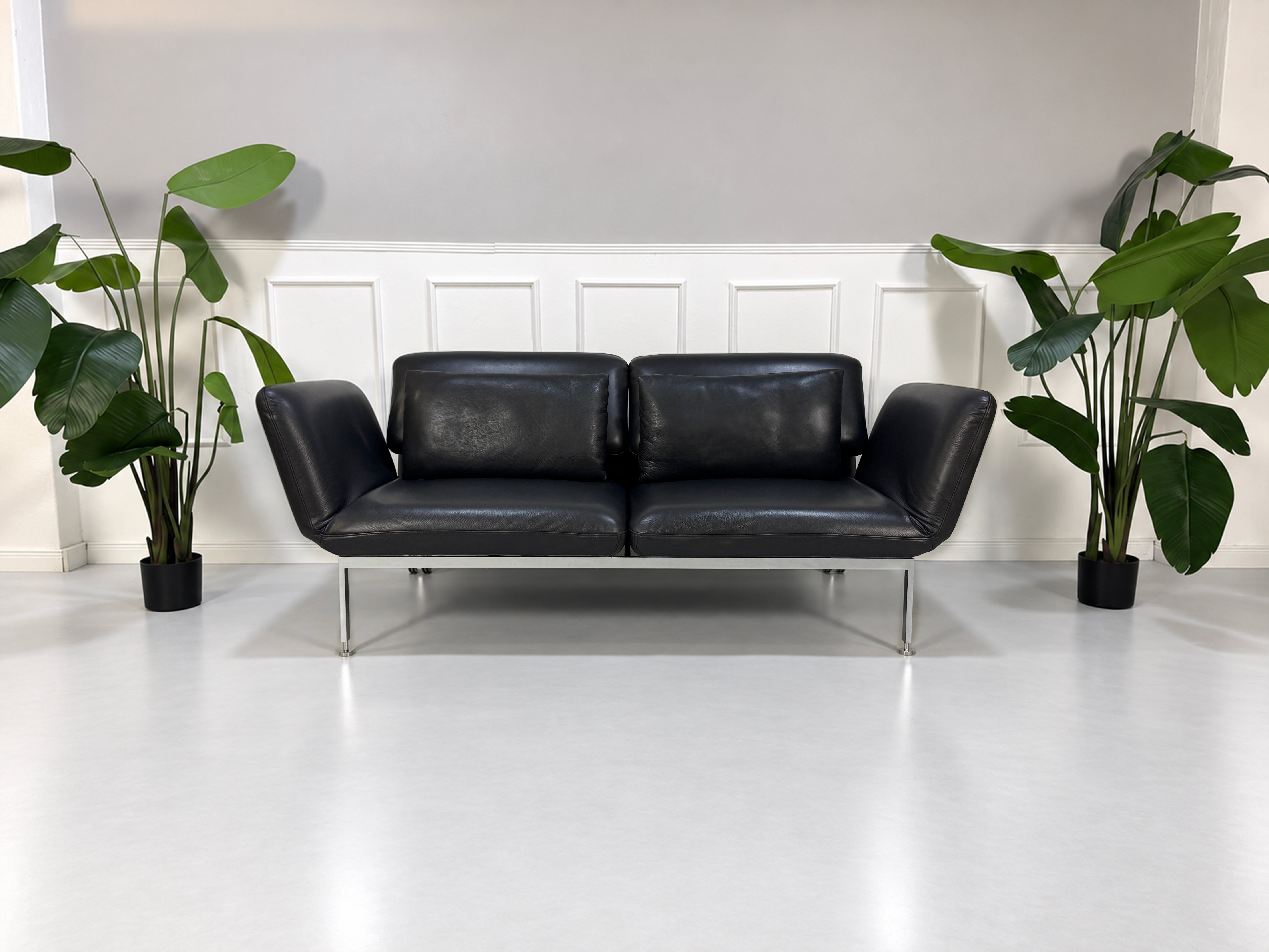 Gebrauchtes graues Brühl Roro Medium Designer Leder Sofa vor einer Wand, stilvoll und modern eingerichtet.