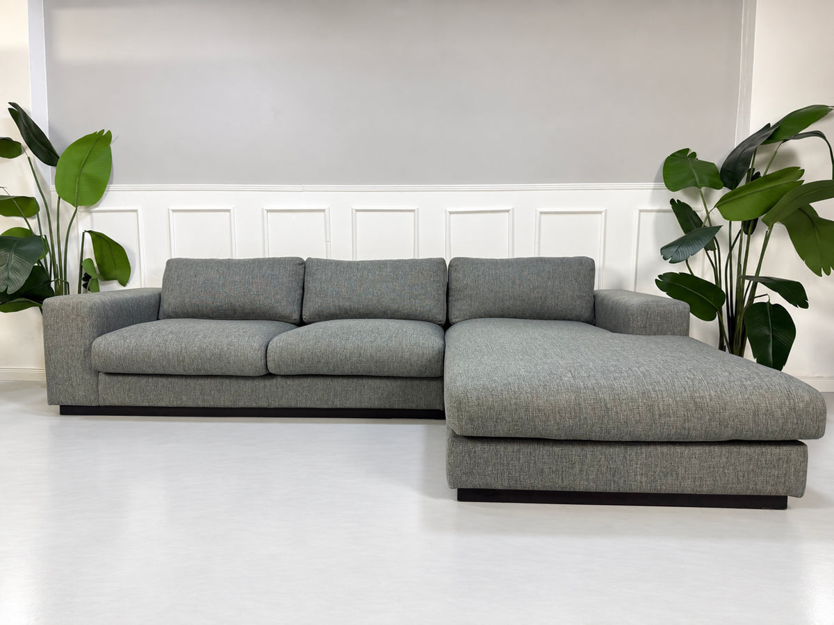 Gebrauchtes graues Bolia Sepia Designer Stoff Ecksofa vor einer Wand, stilvoll und modern eingerichtet.