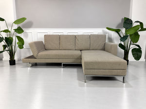 Gebrauchtes grau-beiges Brühl Fourtwo Designer Stoff Ecksofa vor einer Wand, stilvoll und modern eingerichtet.