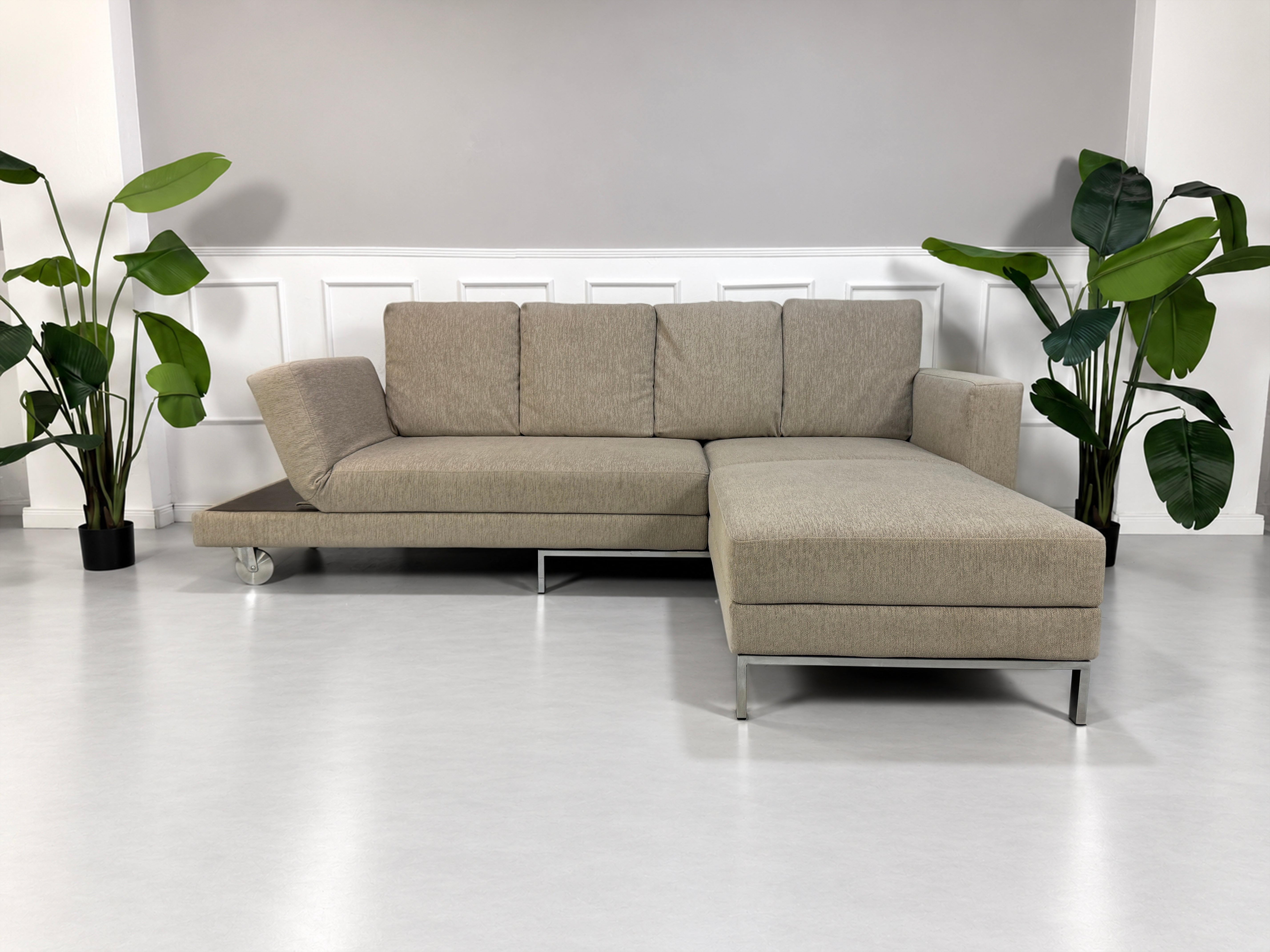 Gebrauchtes grau-beiges Brühl Fourtwo Designer Stoff Ecksofa vor einer Wand, stilvoll und modern eingerichtet.