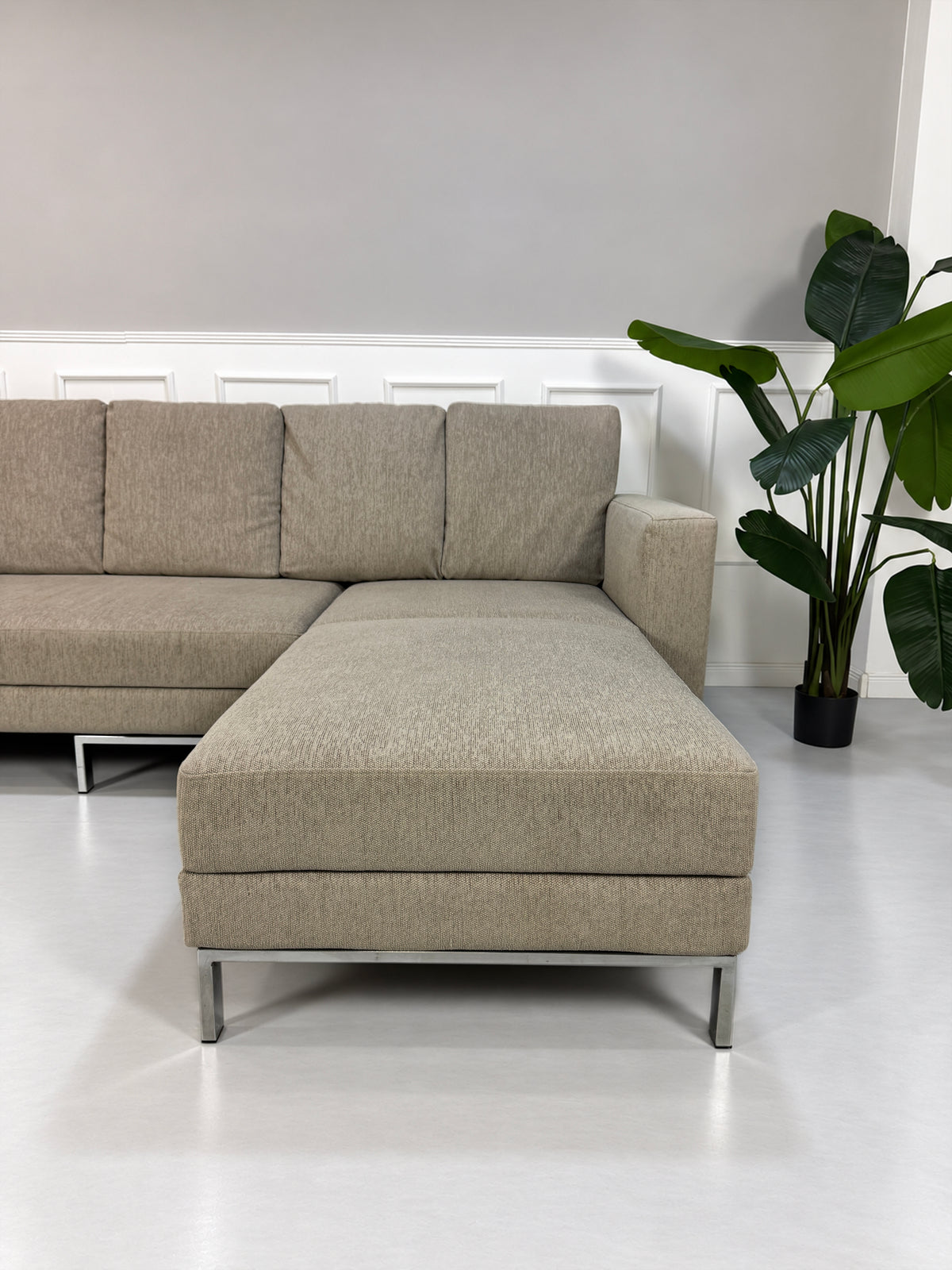 Gebrauchtes grau-beiges Brühl Fourtwo Designer Stoff Ecksofa vor einer Wand, stilvoll und modern eingerichtet.