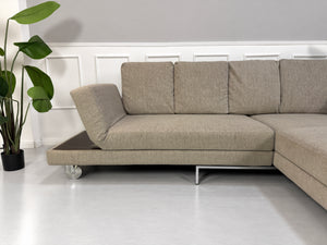 Gebrauchtes grau-beiges Brühl Fourtwo Designer Stoff Ecksofa vor einer Wand, stilvoll und modern eingerichtet.