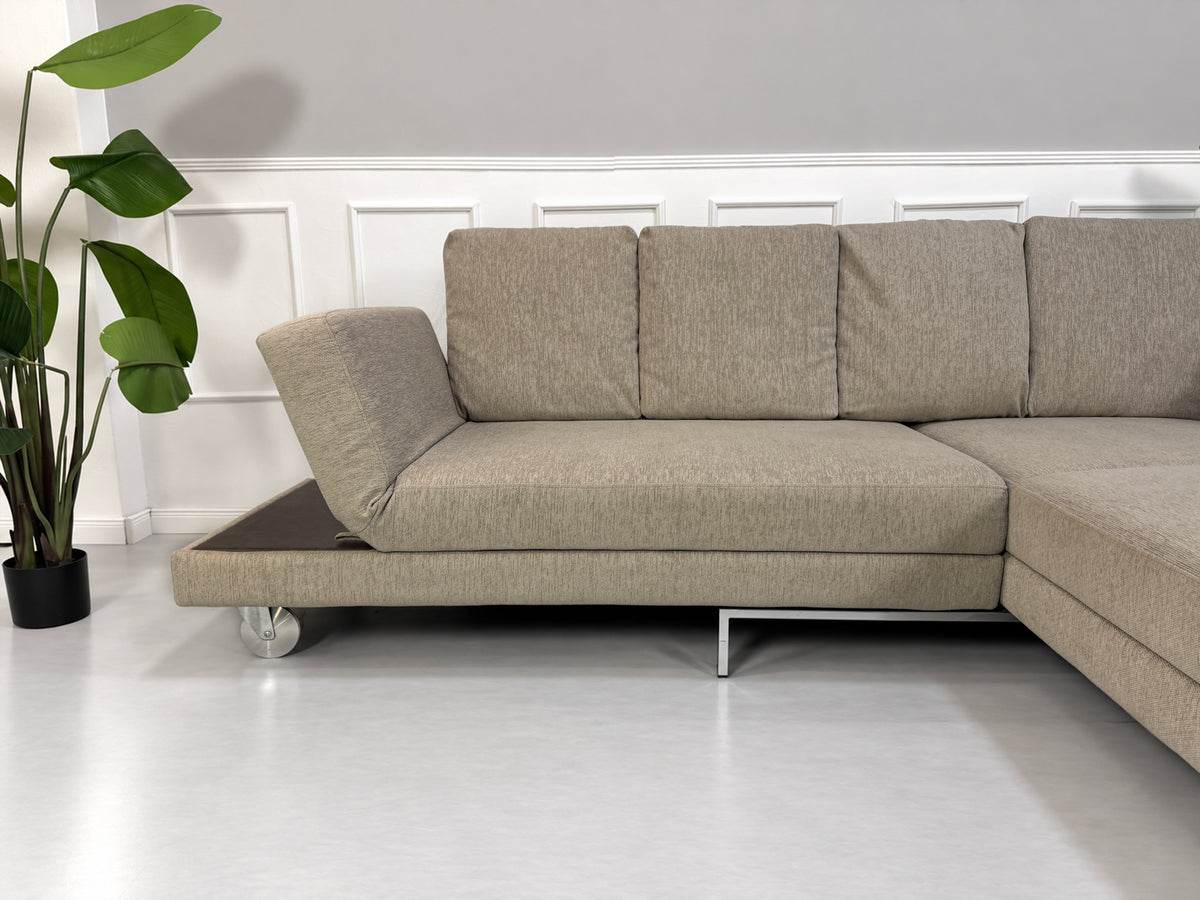 Gebrauchtes grau-beiges Brühl Fourtwo Designer Stoff Ecksofa vor einer Wand, stilvoll und modern eingerichtet.