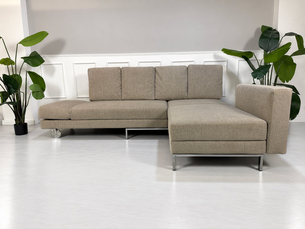 Gebrauchtes grau-beiges Brühl Fourtwo Designer Stoff Ecksofa vor einer Wand, stilvoll und modern eingerichtet.