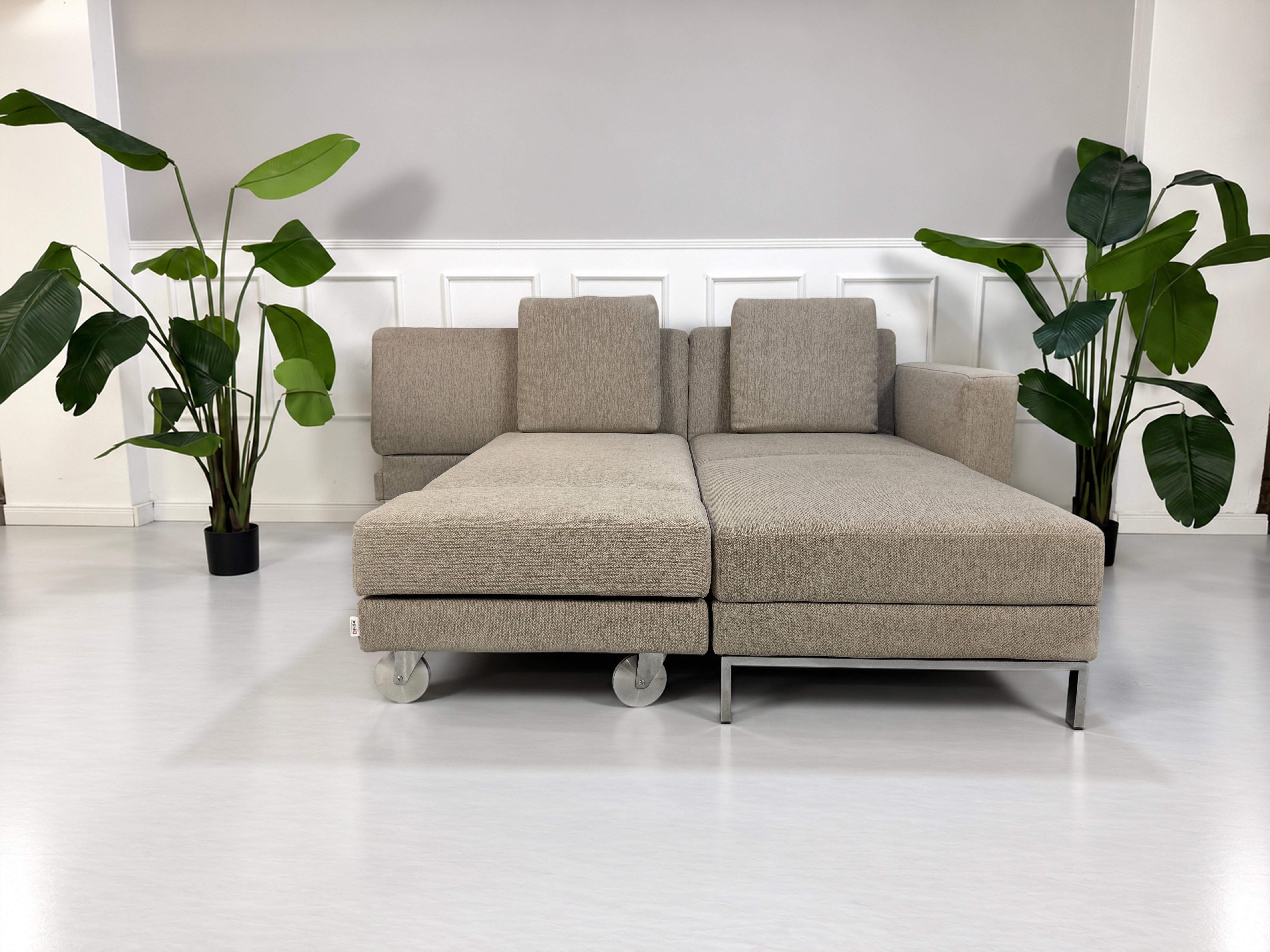 Gebrauchtes grau-beiges Brühl Fourtwo Designer Stoff Ecksofa vor einer Wand, stilvoll und modern eingerichtet.