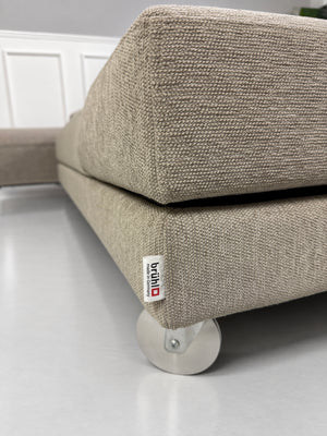 Gebrauchtes grau-beiges Brühl Fourtwo Designer Stoff Ecksofa vor einer Wand, stilvoll und modern eingerichtet.