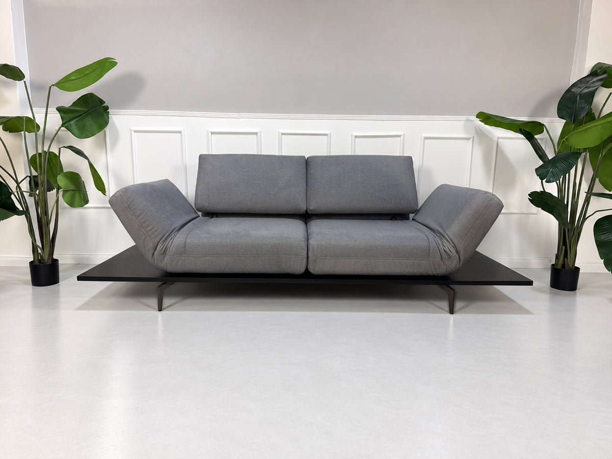 Gebrauchtes grau-blaues Rolf Benz Aura Designer Stoff Sofa vor einer Wand, stilvoll und modern eingerichtet.