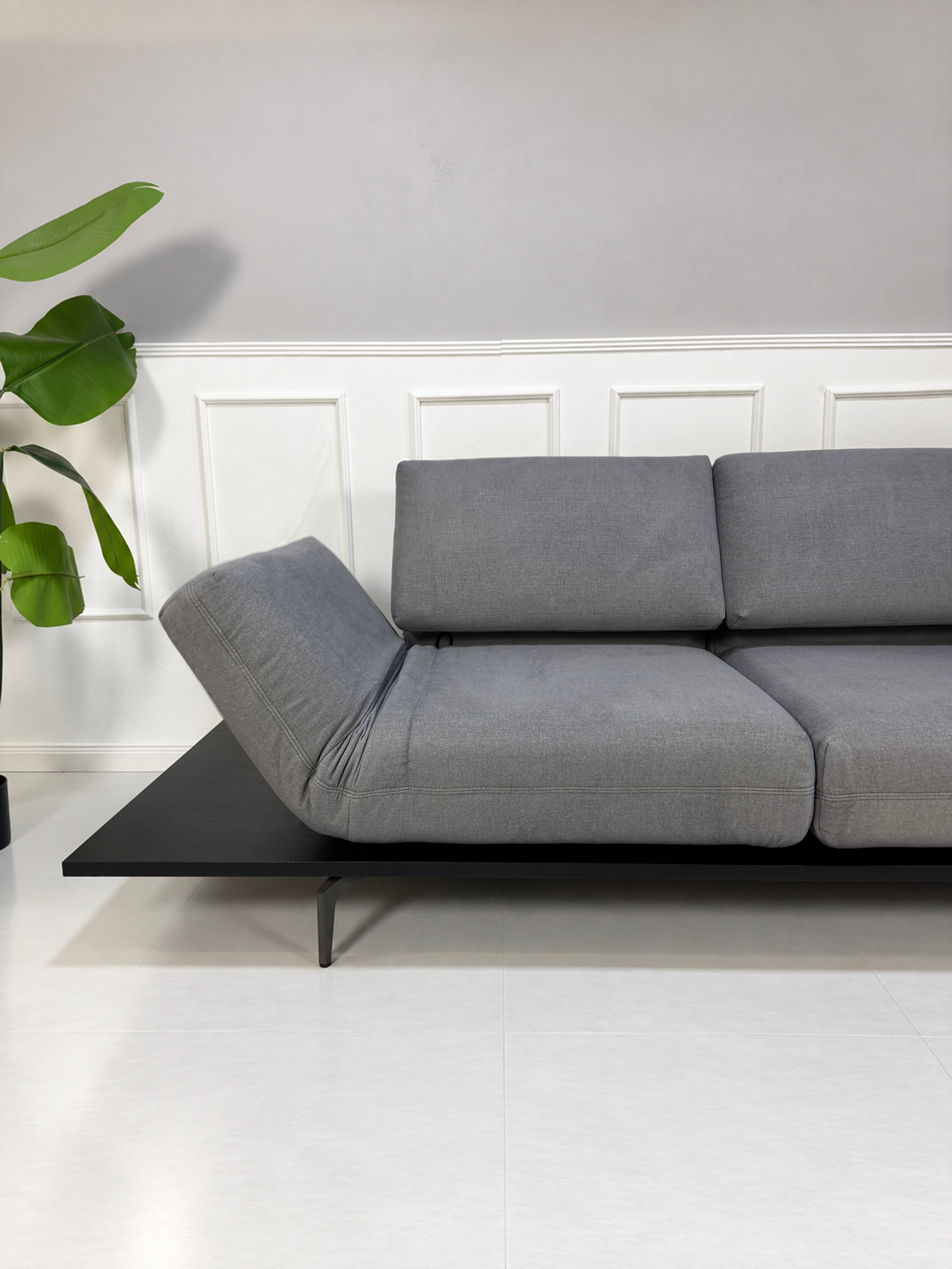 Gebrauchtes grau-blaues Rolf Benz Aura Designer Stoff Sofa vor einer Wand, stilvoll und modern eingerichtet.