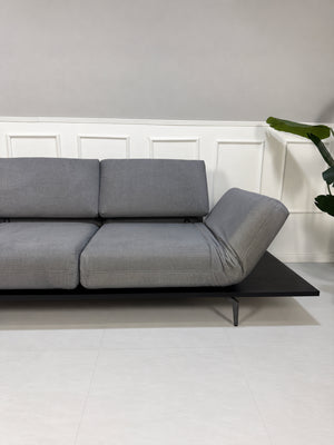 Gebrauchtes grau-blaues Rolf Benz Aura Designer Stoff Sofa vor einer Wand, stilvoll und modern eingerichtet.