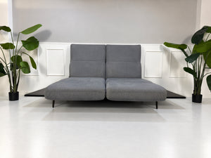 Gebrauchtes grau-blaues Rolf Benz Aura Designer Stoff Sofa vor einer Wand, stilvoll und modern eingerichtet.