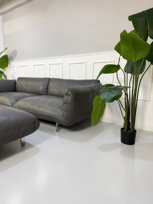 Gebrauchtes graues COR Jalis Designer Leder Sofa mit Hocker vor einer Wand, stilvoll und modern eingerichtet.