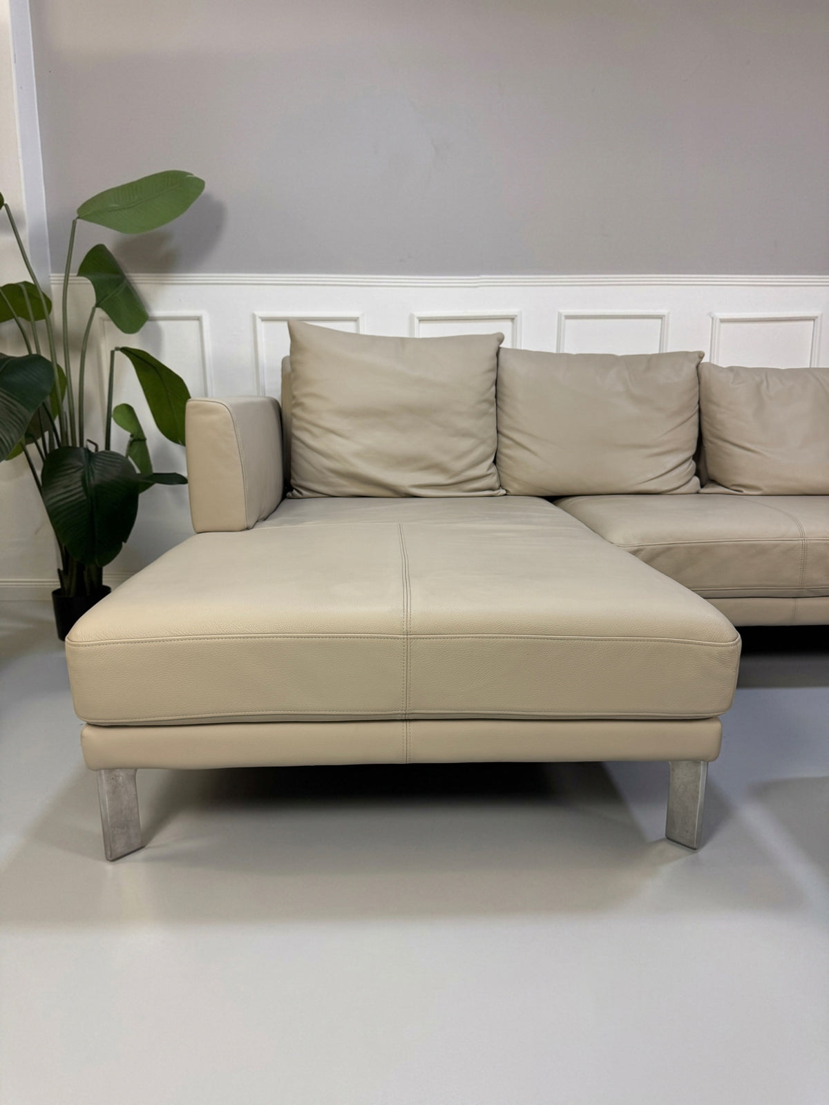 Gebrauchtes beiges Rolf Benz Sento 344 Designer Leder Ecksofa mit Hockerbank vor einer Wand, stilvoll und modern eingerichtet.