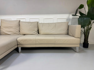 Gebrauchtes beiges Rolf Benz Sento 344 Designer Leder Ecksofa mit Hockerbank vor einer Wand, stilvoll und modern eingerichtet.
