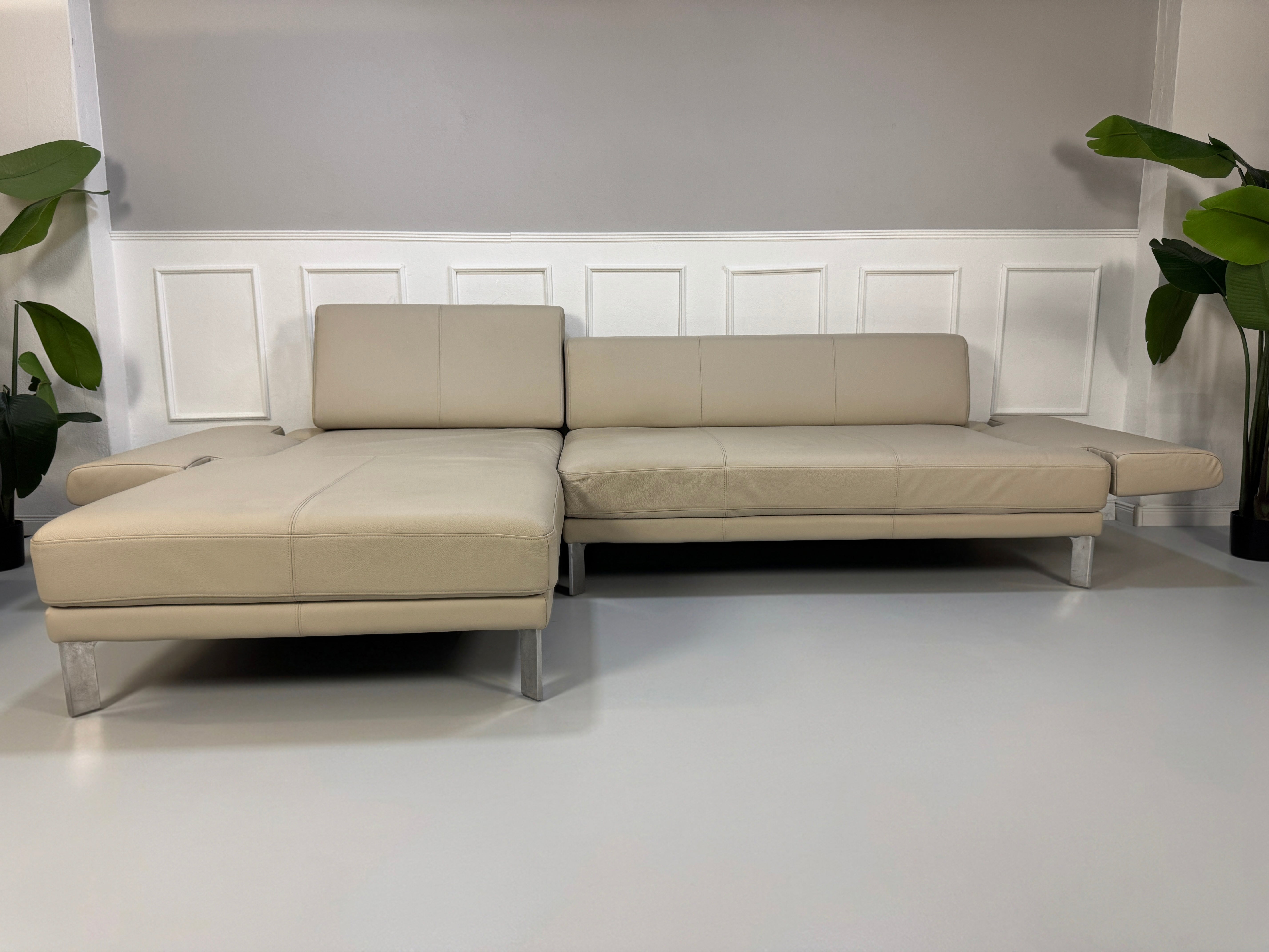 Gebrauchtes beiges Rolf Benz Sento 344 Designer Leder Ecksofa mit Hockerbank vor einer Wand, stilvoll und modern eingerichtet.