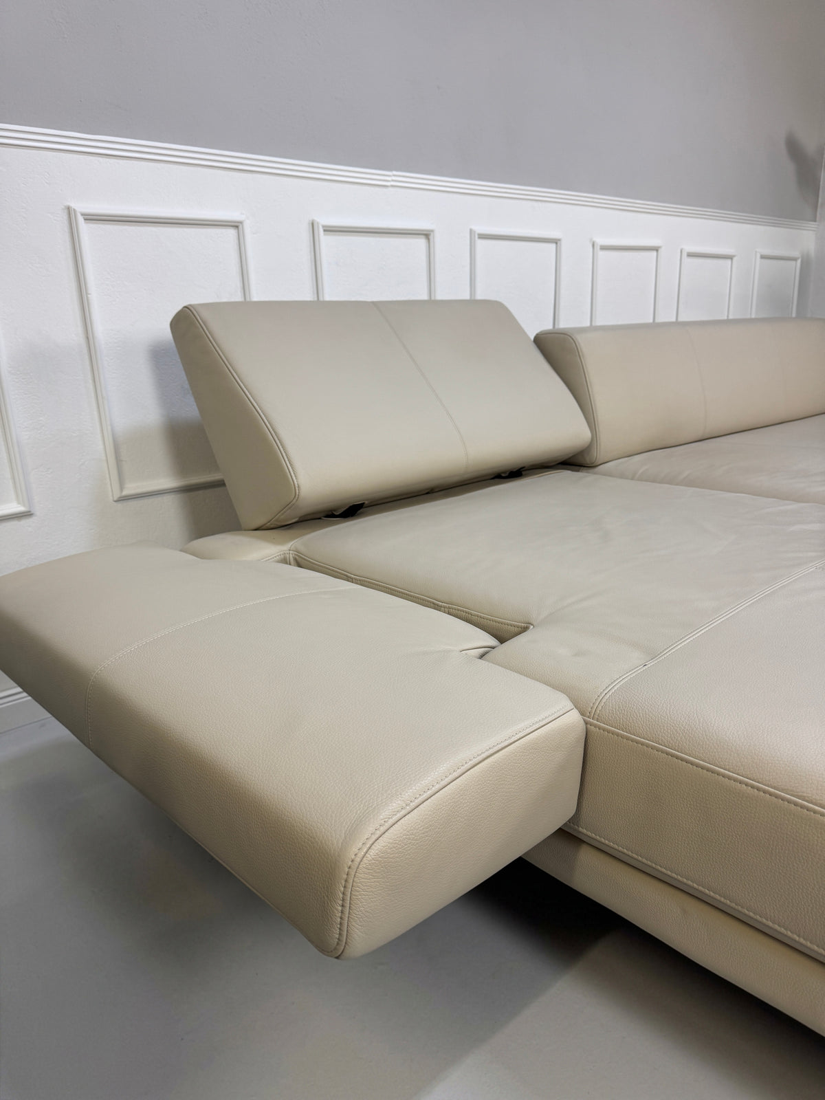 Gebrauchtes beiges Rolf Benz Sento 344 Designer Leder Ecksofa mit Hockerbank vor einer Wand, stilvoll und modern eingerichtet.