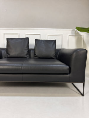 Gebrauchtes schwarzes COR Mell Designer Leder Sofa vor einer Wand, stilvoll und modern eingerichtet.