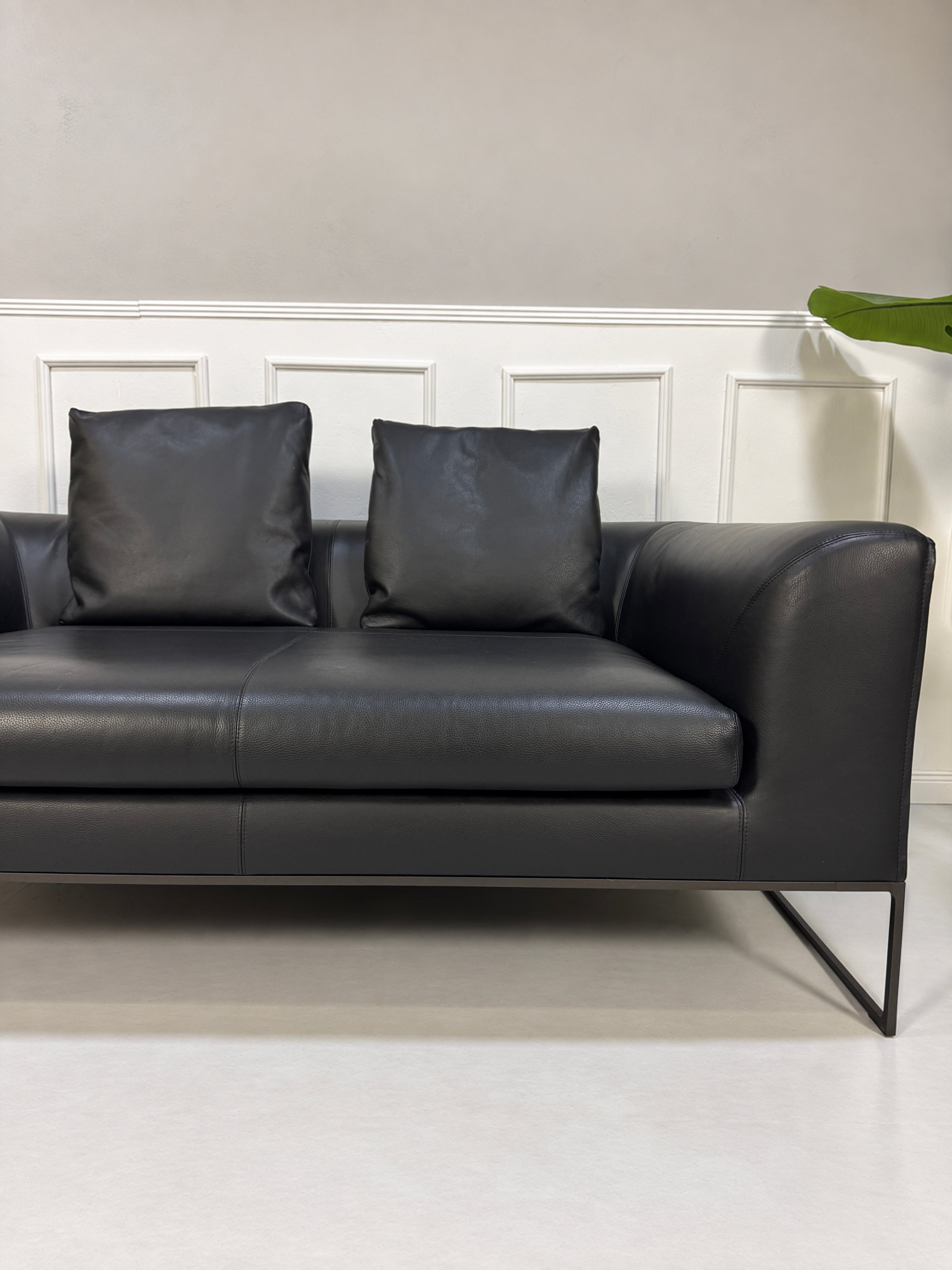 Gebrauchtes schwarzes COR Mell Designer Leder Sofa vor einer Wand, stilvoll und modern eingerichtet.