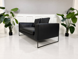 Gebrauchtes schwarzes COR Mell Designer Leder Sofa vor einer Wand, stilvoll und modern eingerichtet.