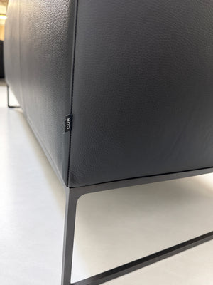 Gebrauchtes schwarzes COR Mell Designer Leder Sofa vor einer Wand, stilvoll und modern eingerichtet.